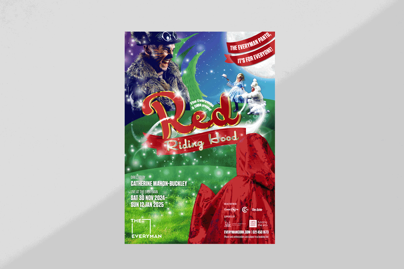 Bright promotional poster for a theatrical production titled 'Red Riding Hood,' directed by Catherine Mahon-Buckley. It features a smiling man in a fur coat and goggles, a girl in a blue dress, and a person in a red hooded cloak standing on a green hill under a large moon.