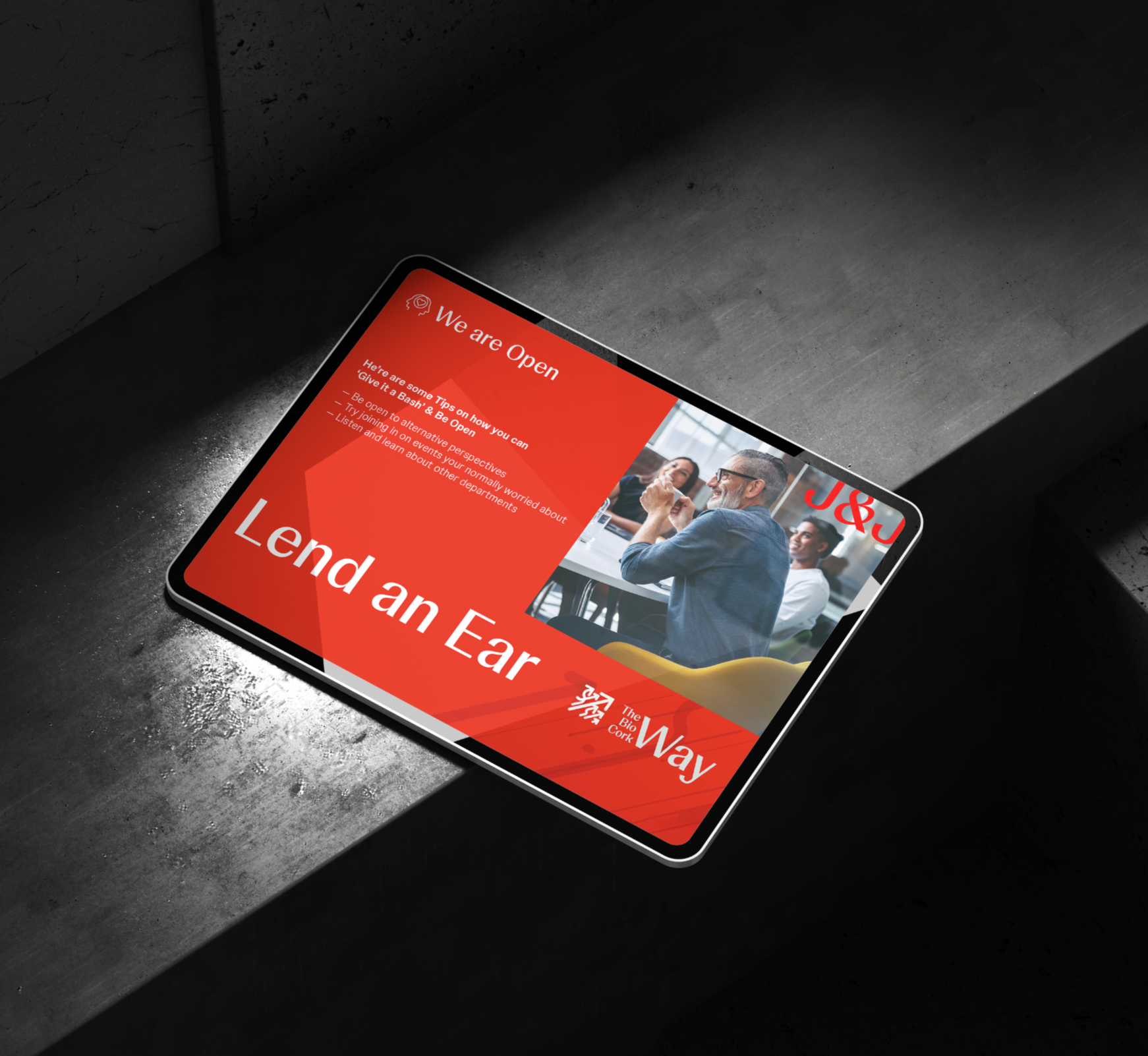 Johnson & Johnson Branded Smartphone on dark surface displaying a webpage with red background, white text saying "We are Open," and an image of people in a meeting.