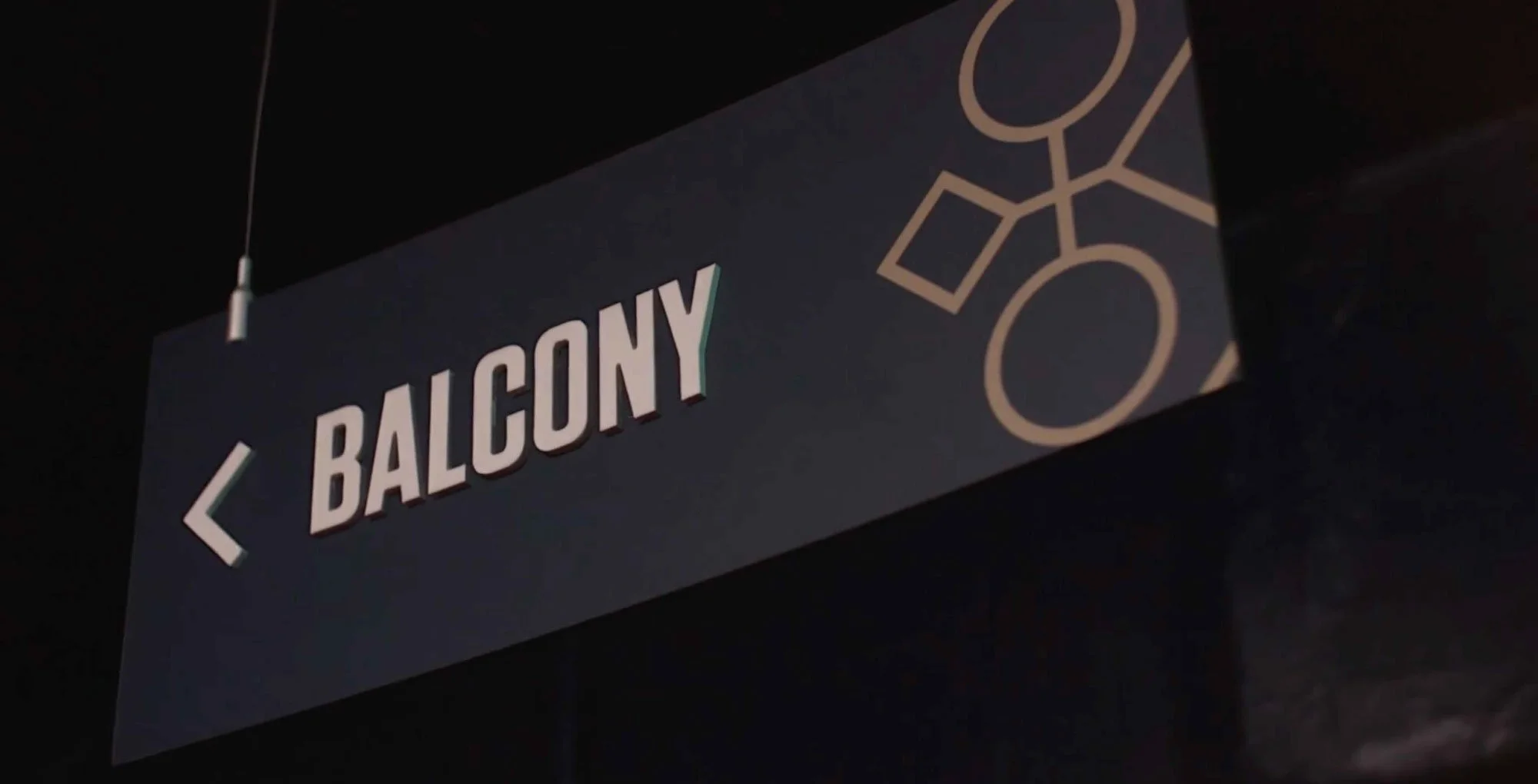 Sign pointing to a balcony with an arrow, featuring a geometric design in neutral tones.