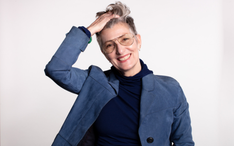 Jeanette Bronée in blue jacket smiling and touching hair