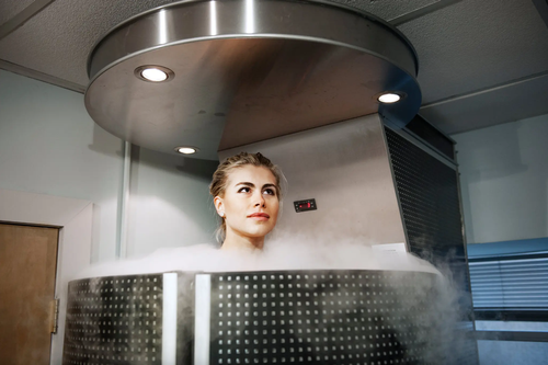 Person inside a cryotherapy chamber with mist surrounding their upper body.