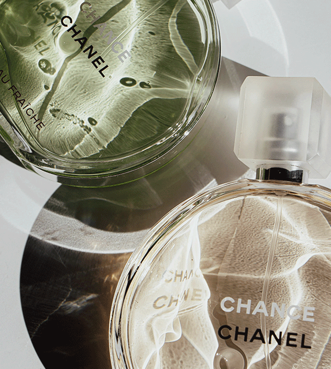 Two bottles of Chanel perfume, one with a clear liquid and another with a pale pink liquid, placed on a reflective surface with light and shadow reflections.