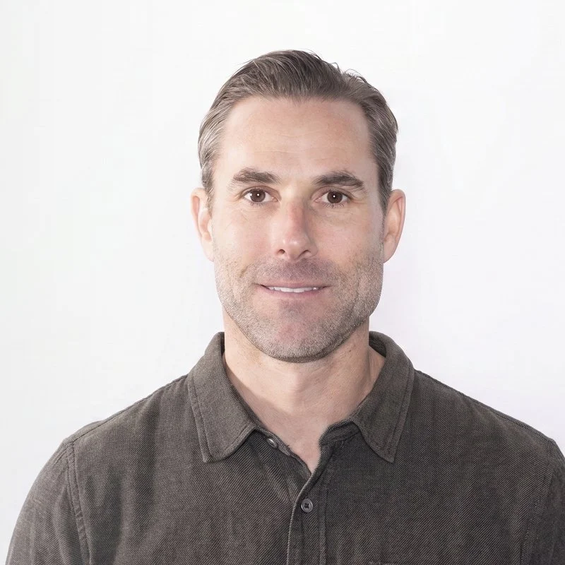 A man named Matt Thomas with short, gray hair and a slight beard, wearing a dark button-up shirt, looks at the camera against a plain white background.