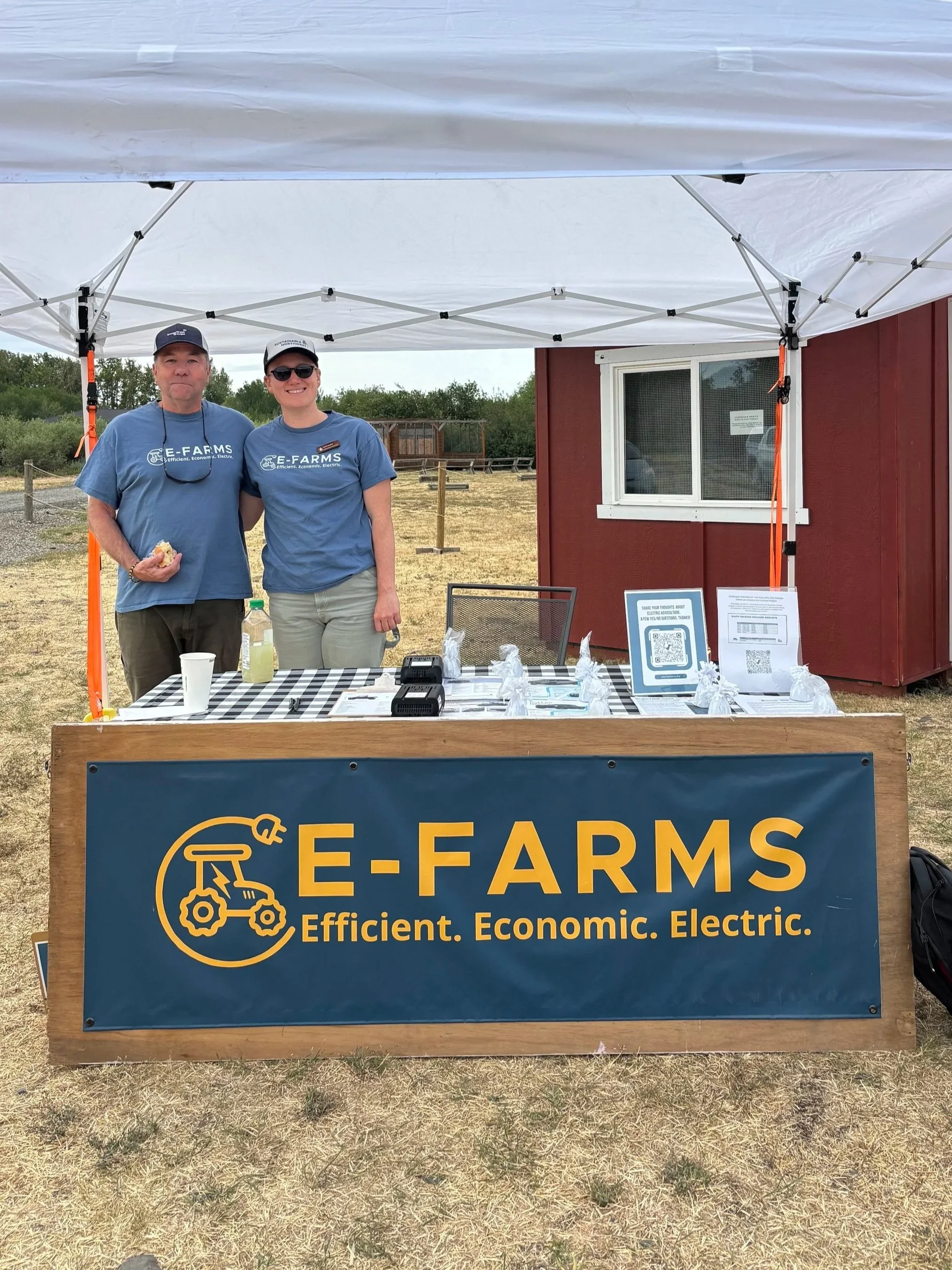  David Skakel and Sarah Gledhill in front of the E-Farms booth at Jensen Farms, sharing information on electric farm equipment with visitors. Photo credit Maia Gutmann. 