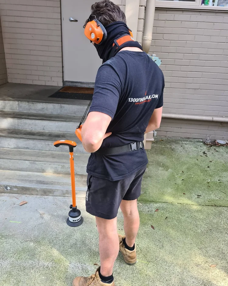 Technician listening for an underground leak with a ground microphone in a garden