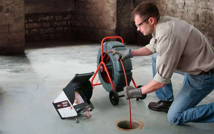 Technician feeding a drain camera into a floor drain
