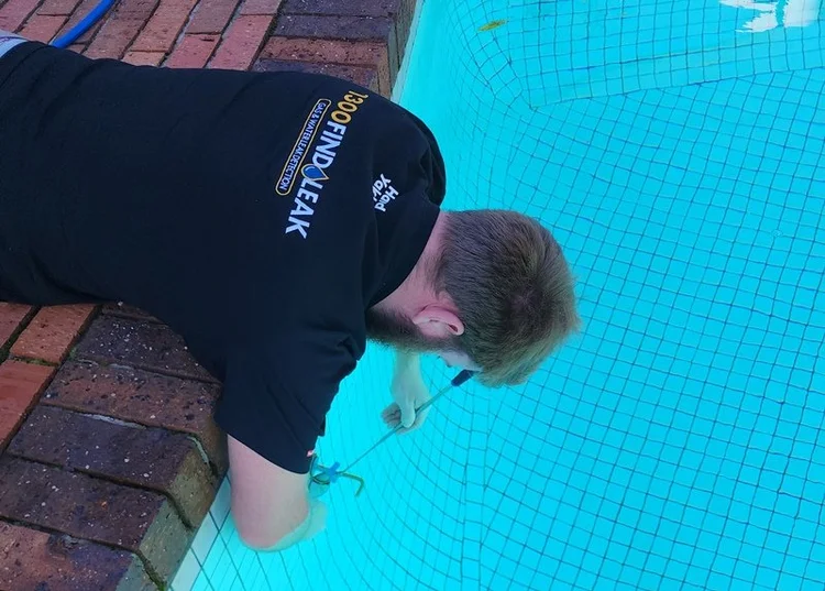 Technician inspecting pool tiles for a leak