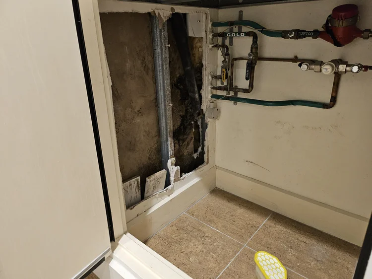 Wall opened behind a shower to expose a leaking pipe