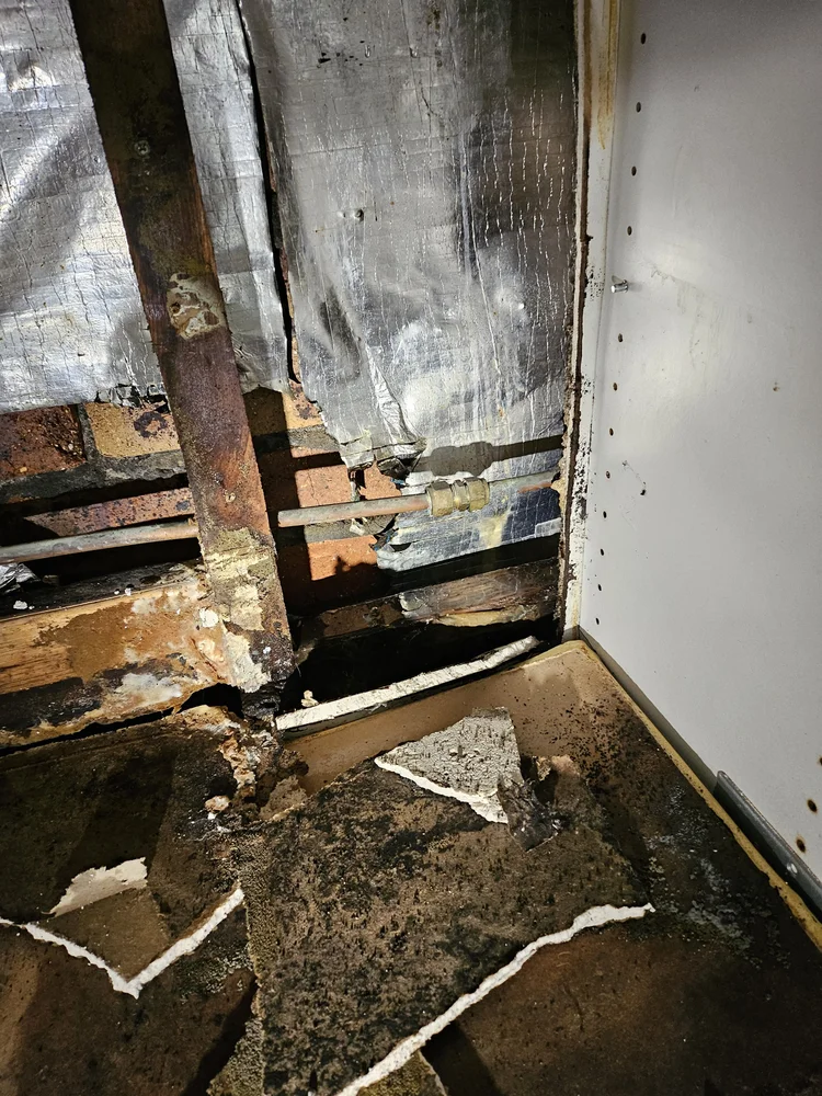Floorboards lifted to expose leaking pipes under a timber floor