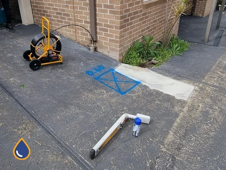 Drain camera reel on a driveway with the pipe location marked in paint