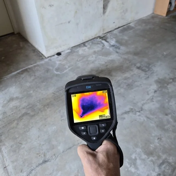 High-resolution thermal imaging camera showing heat signatures of a hidden water leak behind luxury marble wall tiles and custom timber flooring.