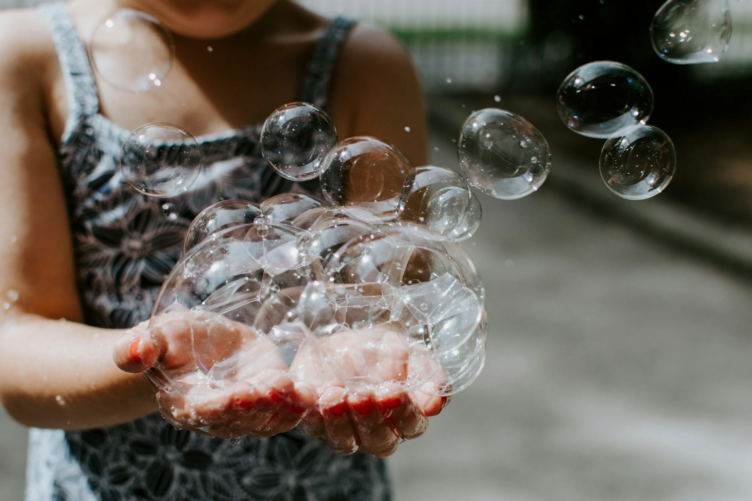 A young girl holding a handful of soap bubbles outdoors.