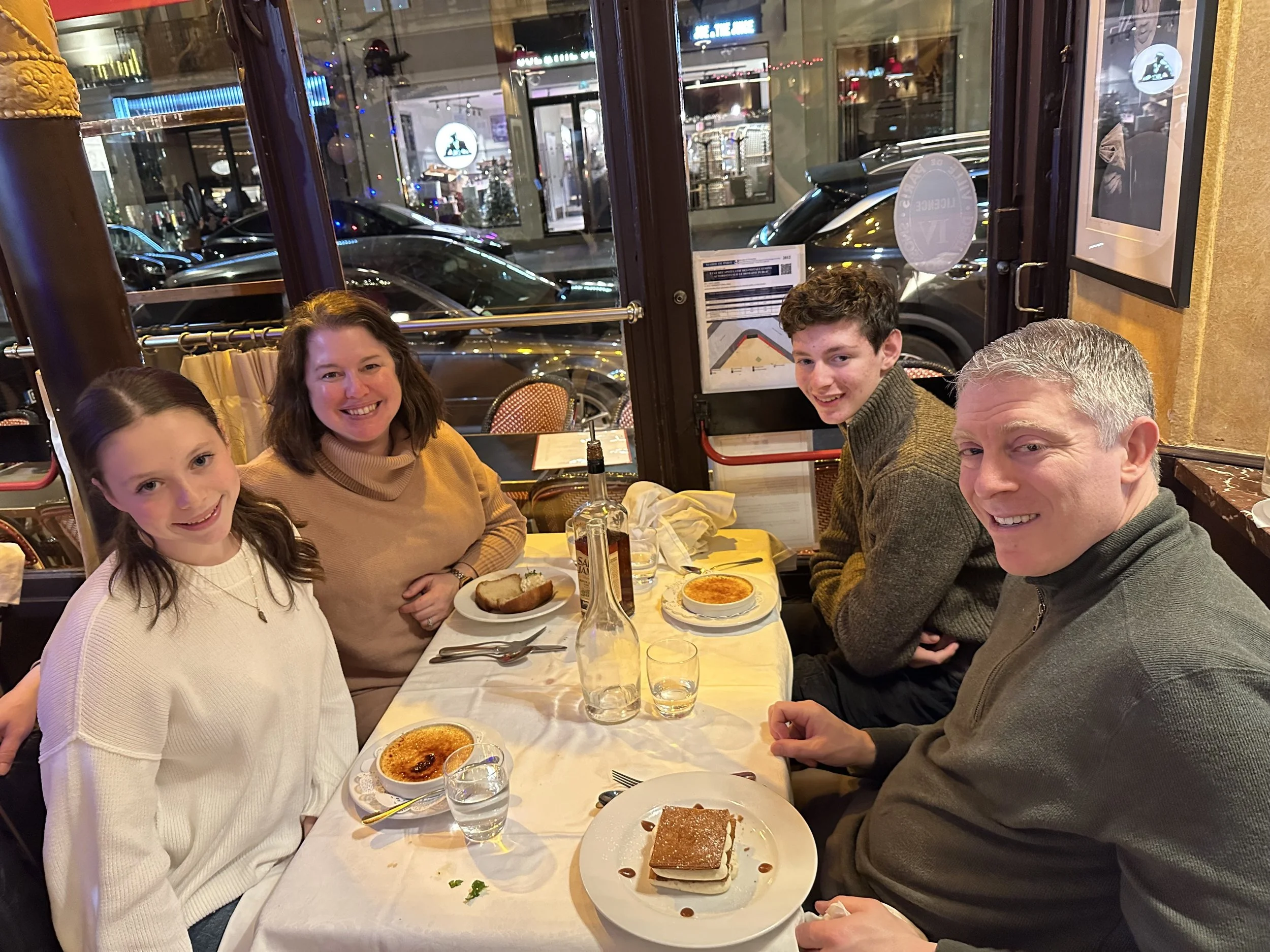 Family of four sitting in a French cafe in Paris after finishing their meal. Dessert is on the table.
