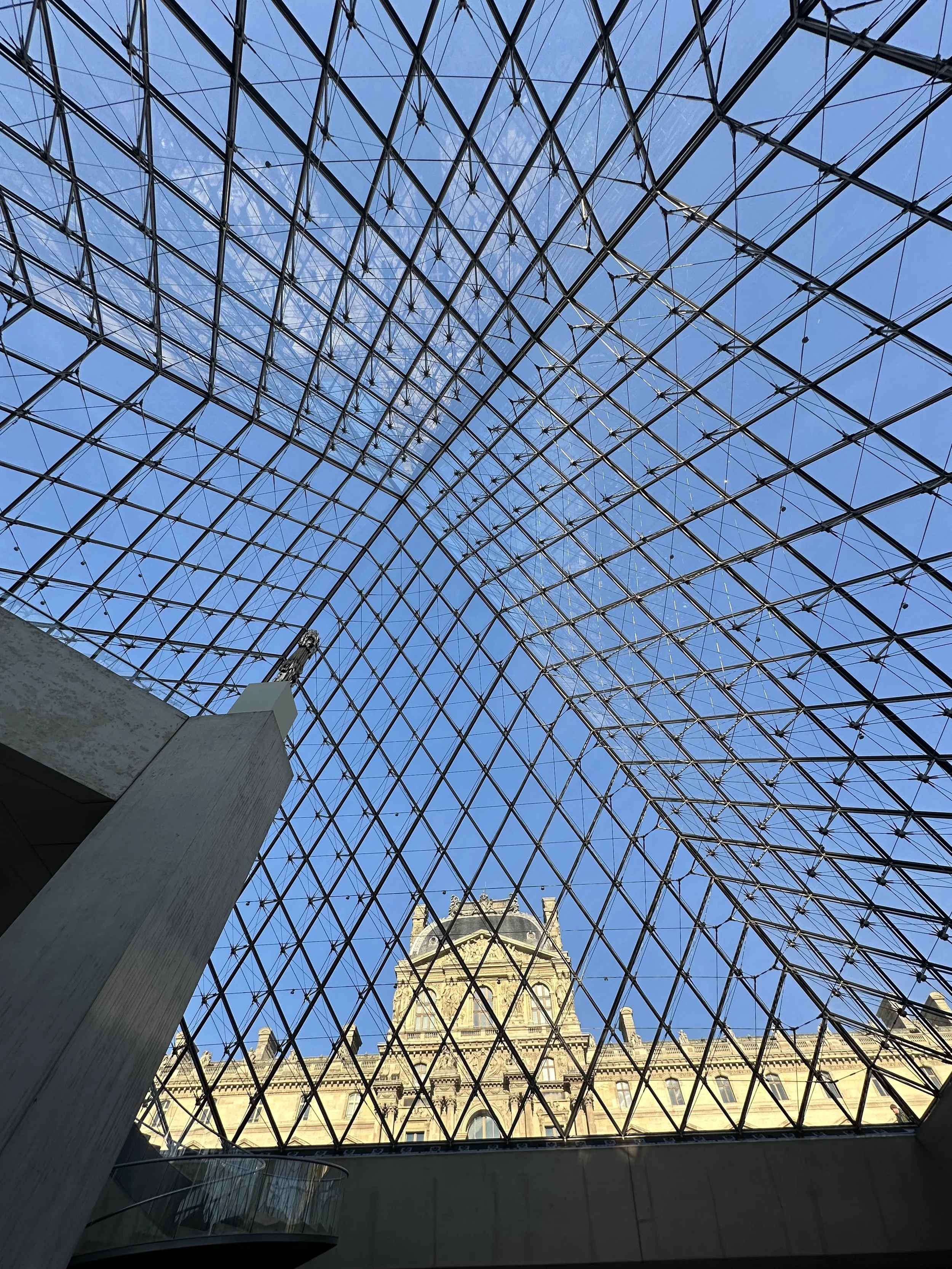 View of the pyramid of the Louvre from inside the museum. It's a sunny, bright blue sky in Paris, France