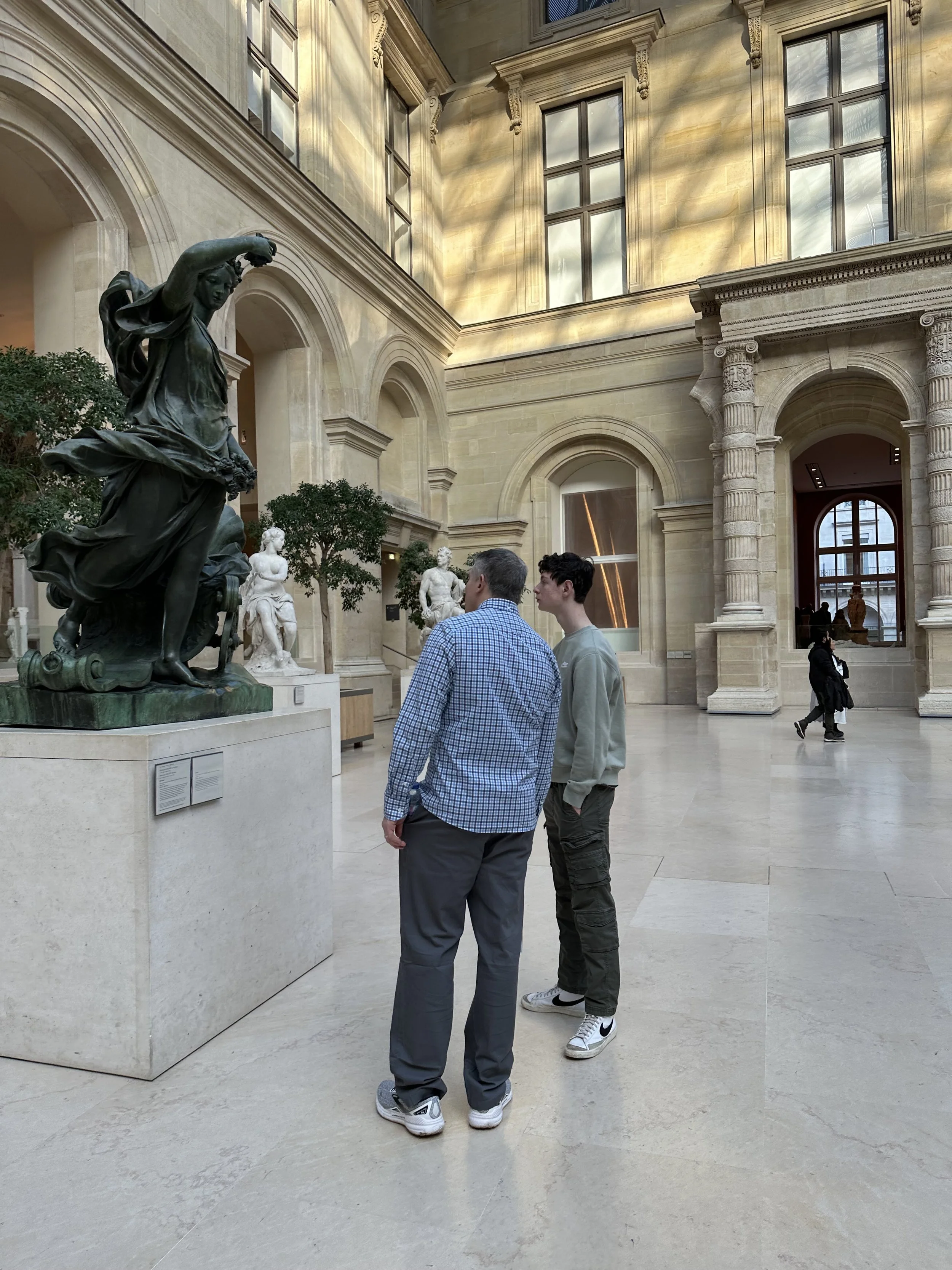Two men at the Louvre reading a plaque at a sculpture in Paris, France