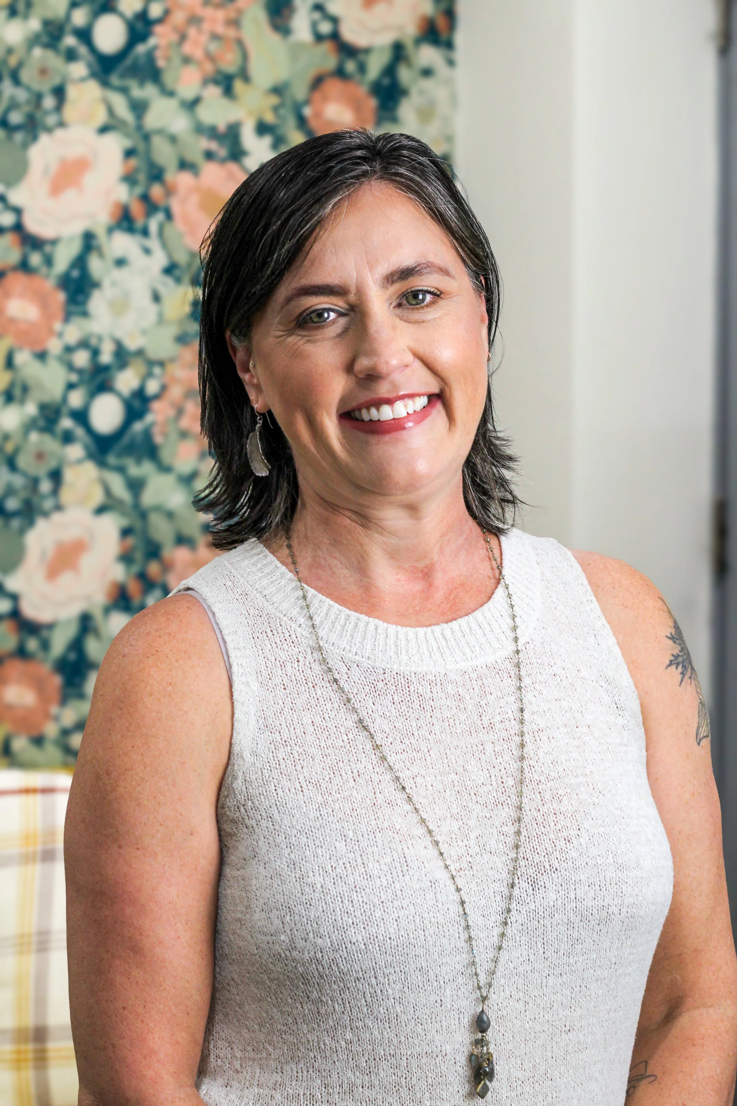 A white woman with dark hair standing in front of a brick wall smiling at the camera. 