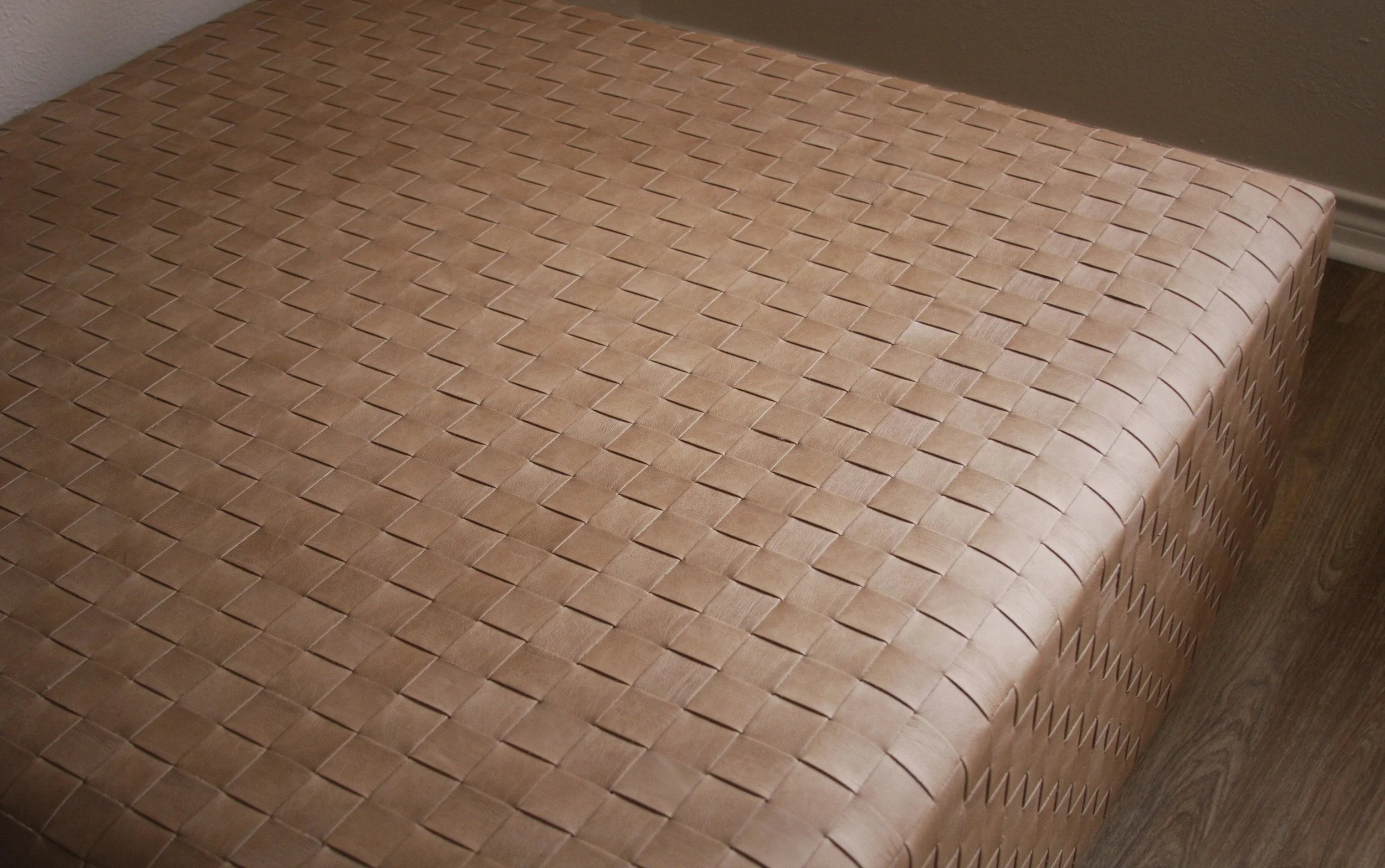 Close-up of a woven wooden furniture piece, likely a bench or table, with a textured pattern and a light wood finish.
