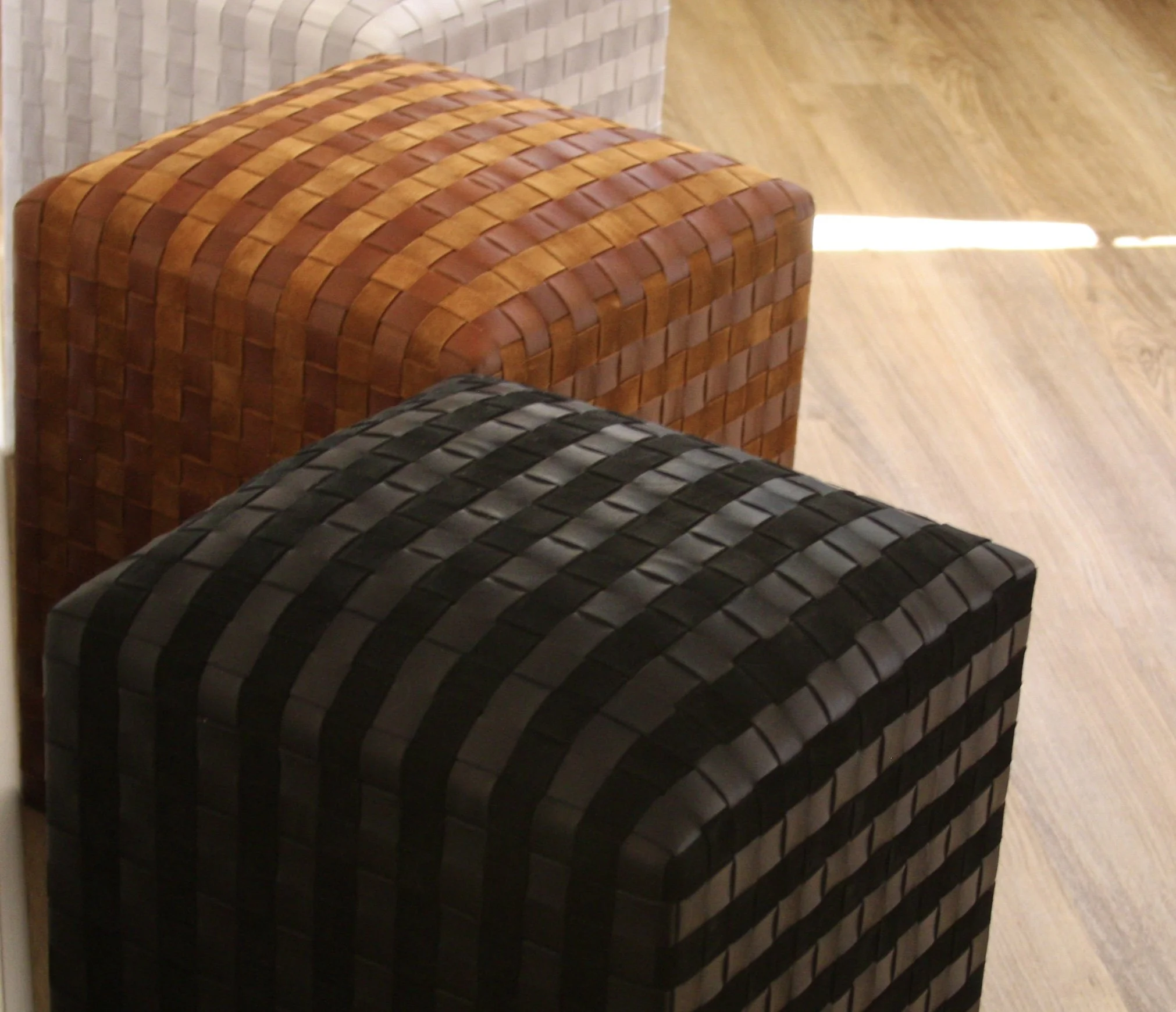 Two woven-pattern ottomans, one in black and one in brown, placed on a wooden floor.
