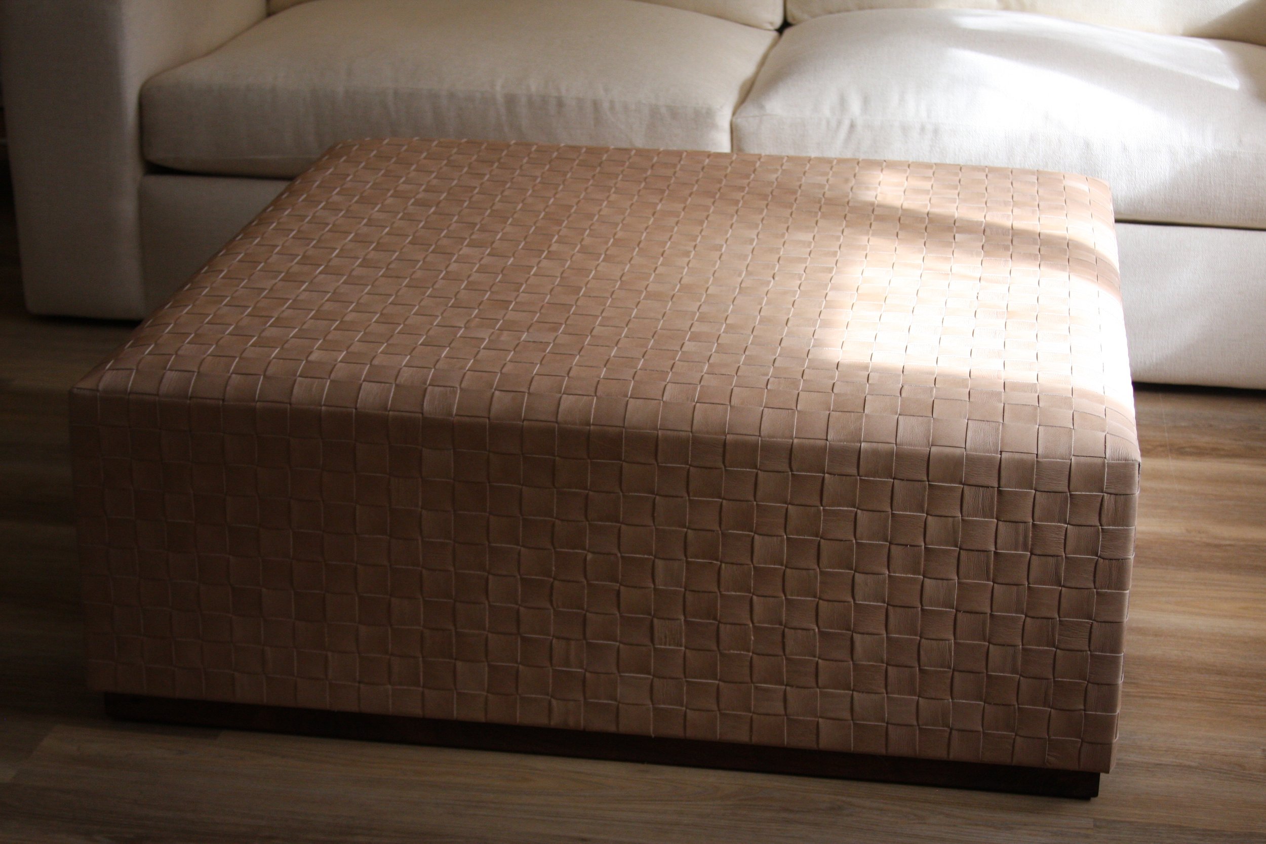 A brown woven-pattern ottoman in front of a beige sofa in a living room.