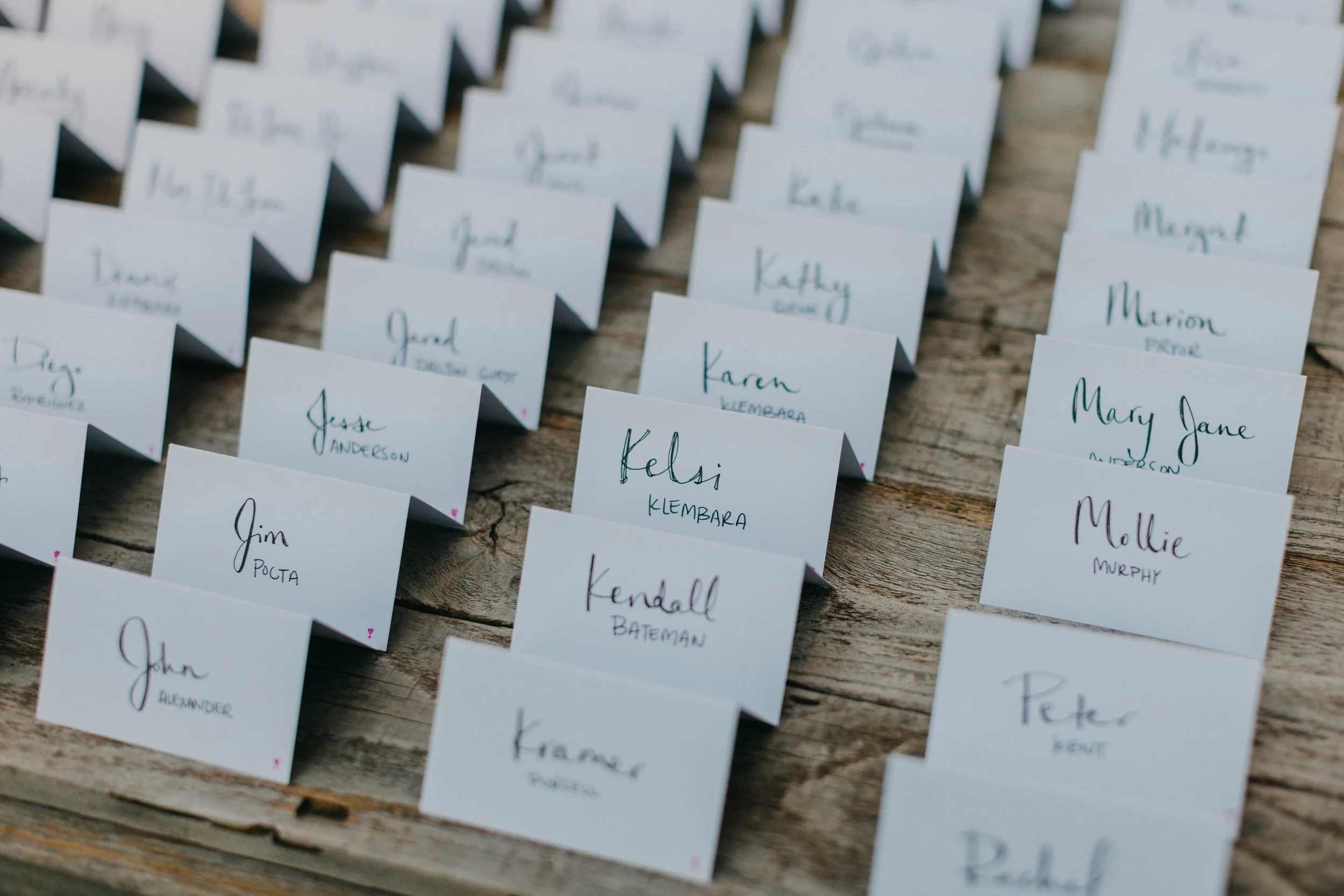 Name cards arranged in a grid on a rustic wooden surface, each card displaying handwritten names.
