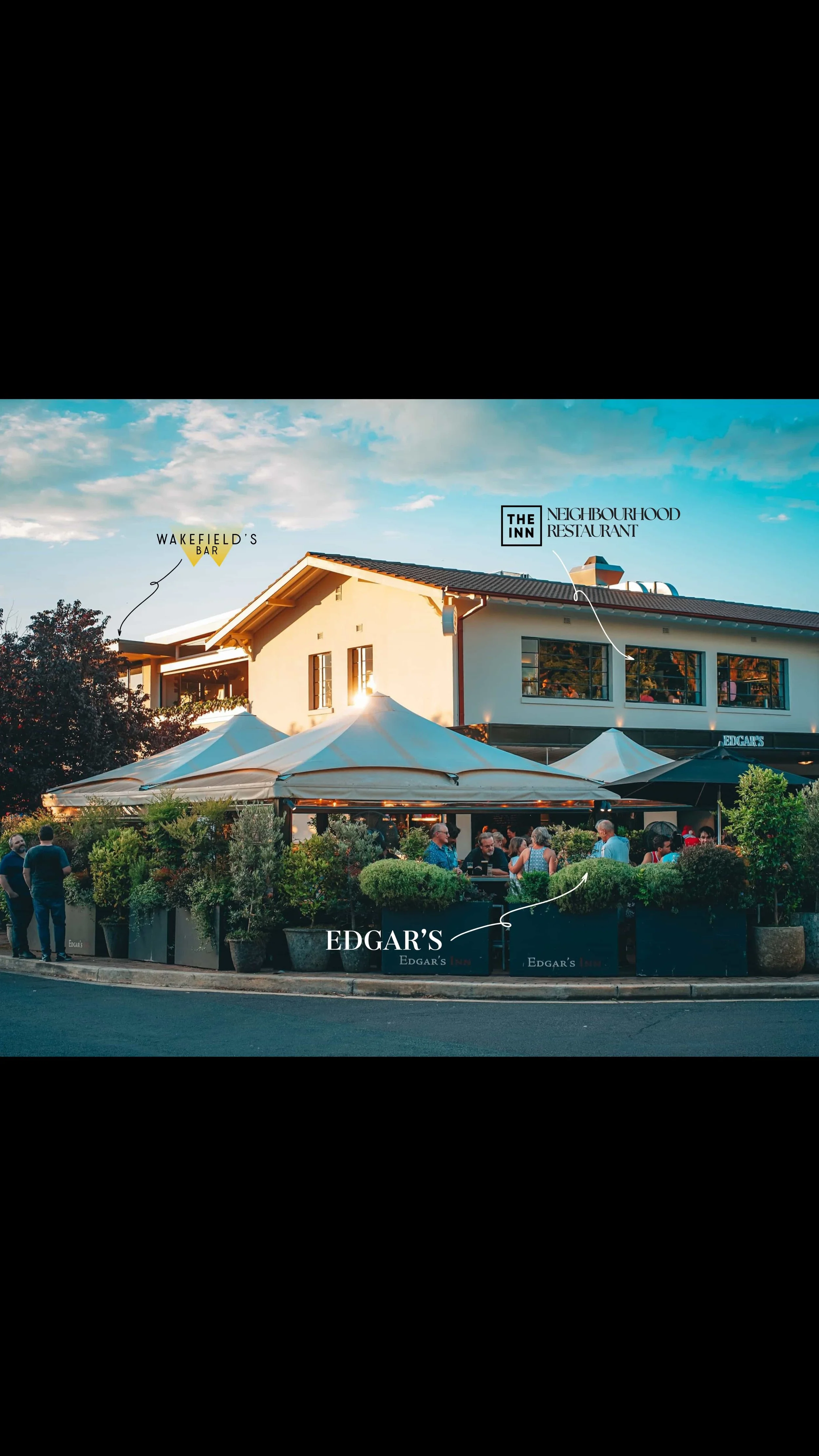 Local Business Edgar's Inn, Ainslie - restaurant outdoor dining area at sunset with white marquee umbrellas and guests dining, Wakefield's Bar and The Inn Restaurant signage visible