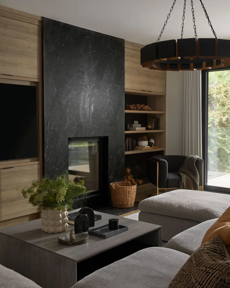 Moody modern living room with black stone fireplace, built-in shelving, neutral seating, and layered textures creating a cozy, elevated interior.