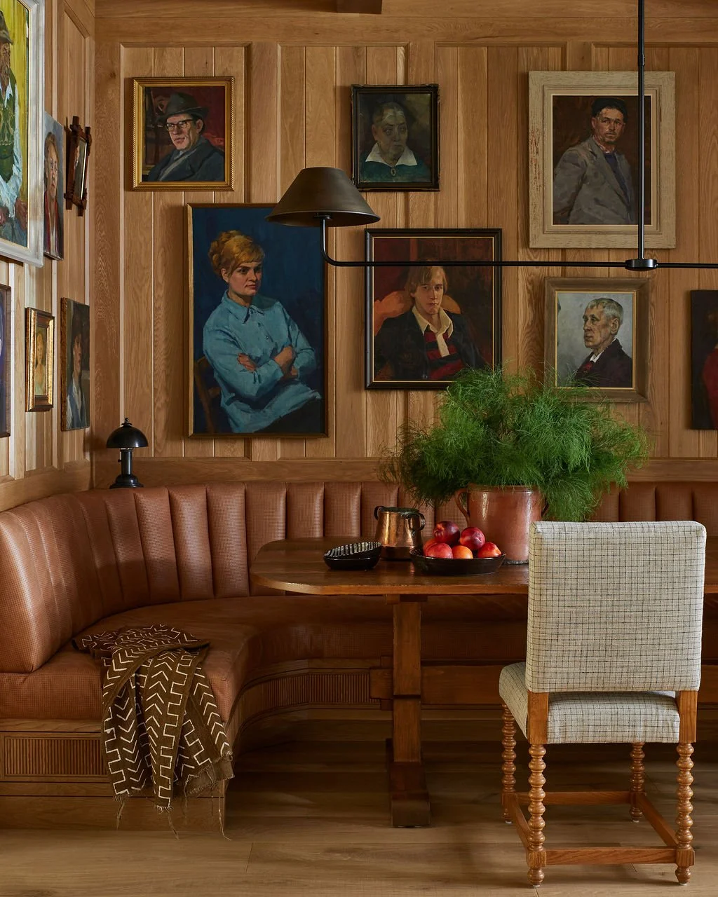 Transitional dining nook with warm wood paneling, leather banquette seating, vintage portrait gallery wall, and layered textures creating a cozy, collected interior.