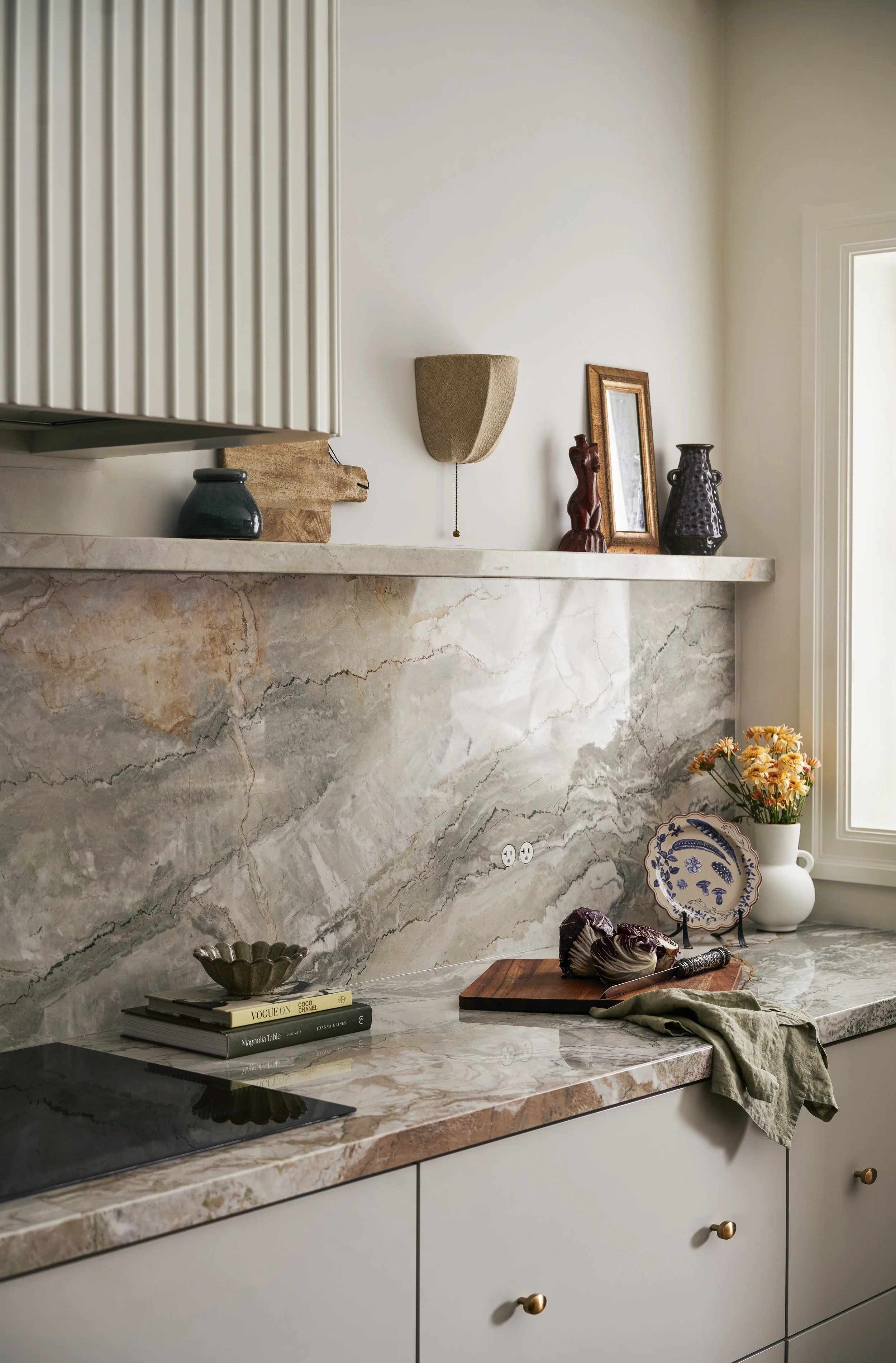 Modern organic kitchen with marble backsplash, fluted cabinetry, styled open shelf, and warm neutral tones highlighting natural materials and texture.