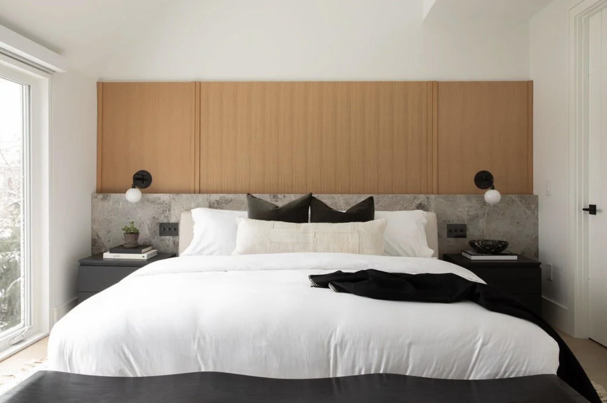 Bright transitional bedroom with high headboard, neutral palette, black metals and modern style nightstand.