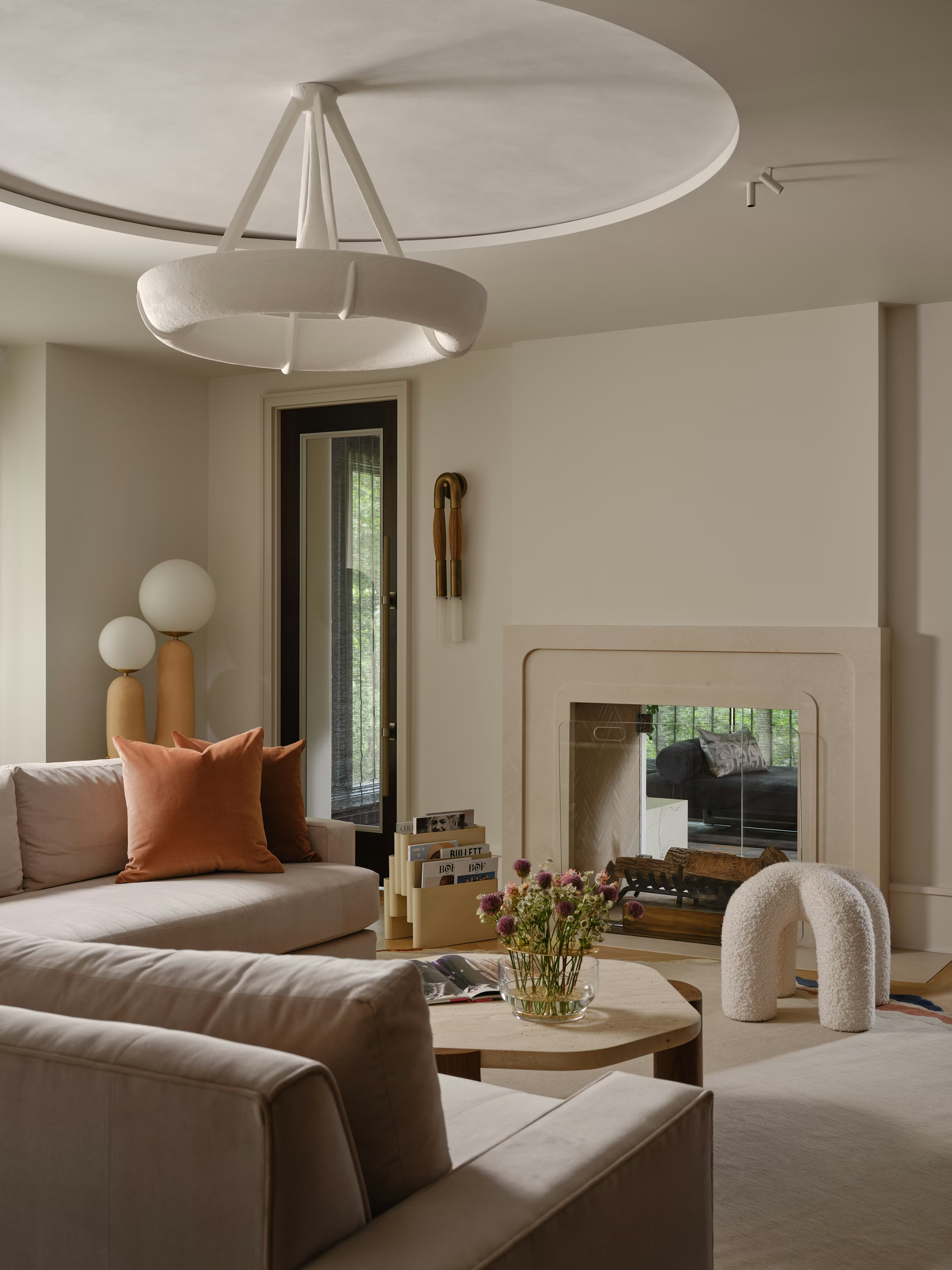 Organic modern living room with curved ceiling detail, sculptural pendant lighting, neutral sofa, and minimalist fireplace creating a calm and elevated space.