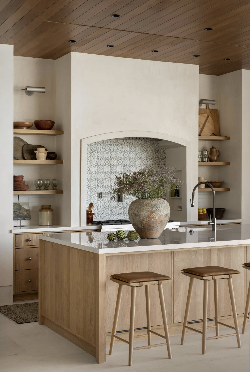 Organic modern kitchen with wood island, plaster range hood, open shelving, and natural materials creating a warm and timeless interior design.