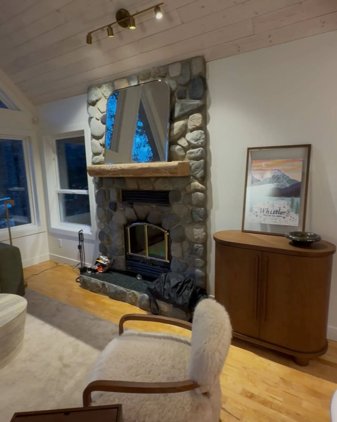 Living room in a Whistler residence featuring a natural stone fireplace, wood mantle, and warm neutral furnishings in a rustic modern style