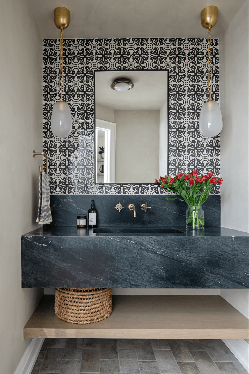 Contemporary powder room featuring bold black-and-white patterned tiles, a floating dark stone vanity, brass fixtures, and glass pendant lights.