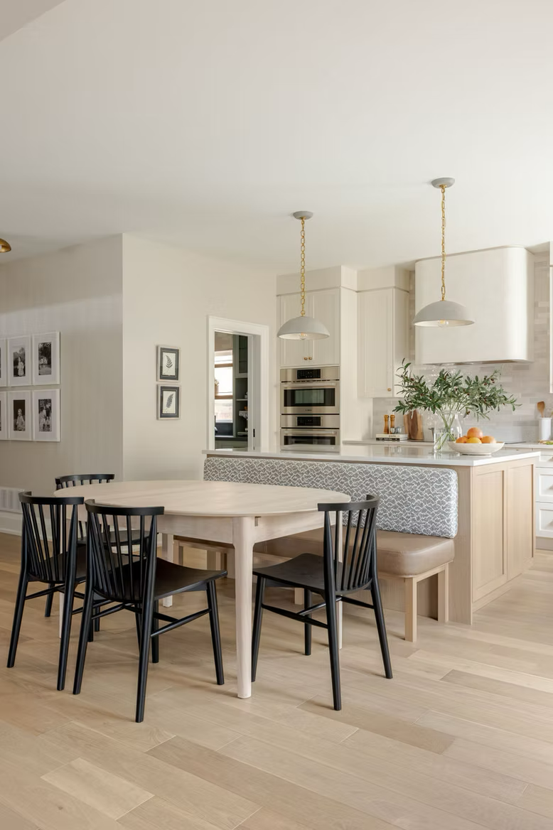 Light transitional dining nook with oval wood table, black accent chairs, soft neutral walls, contemporary shaker style kitchen two toned, and minimalist décor