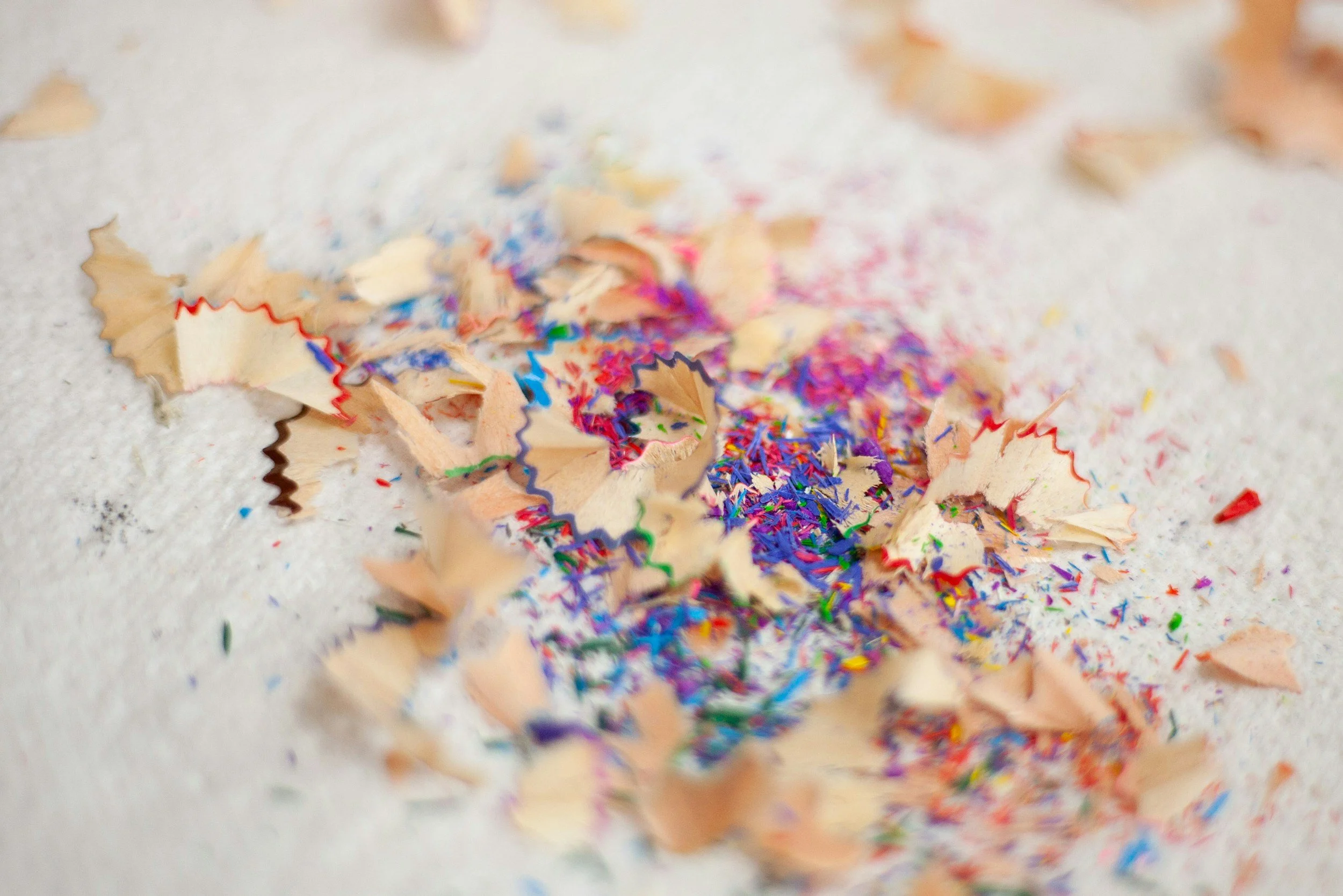 Colorful pencil shavings and tiny pieces of crayon scattered on white surface.