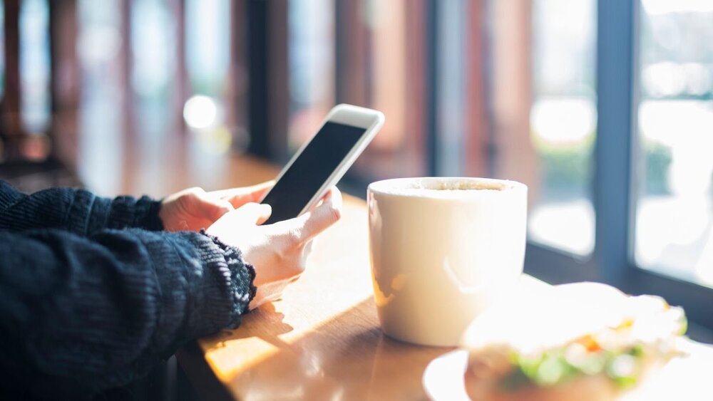 Bilde av kvinne som les på smarttelefonen på kafe. 