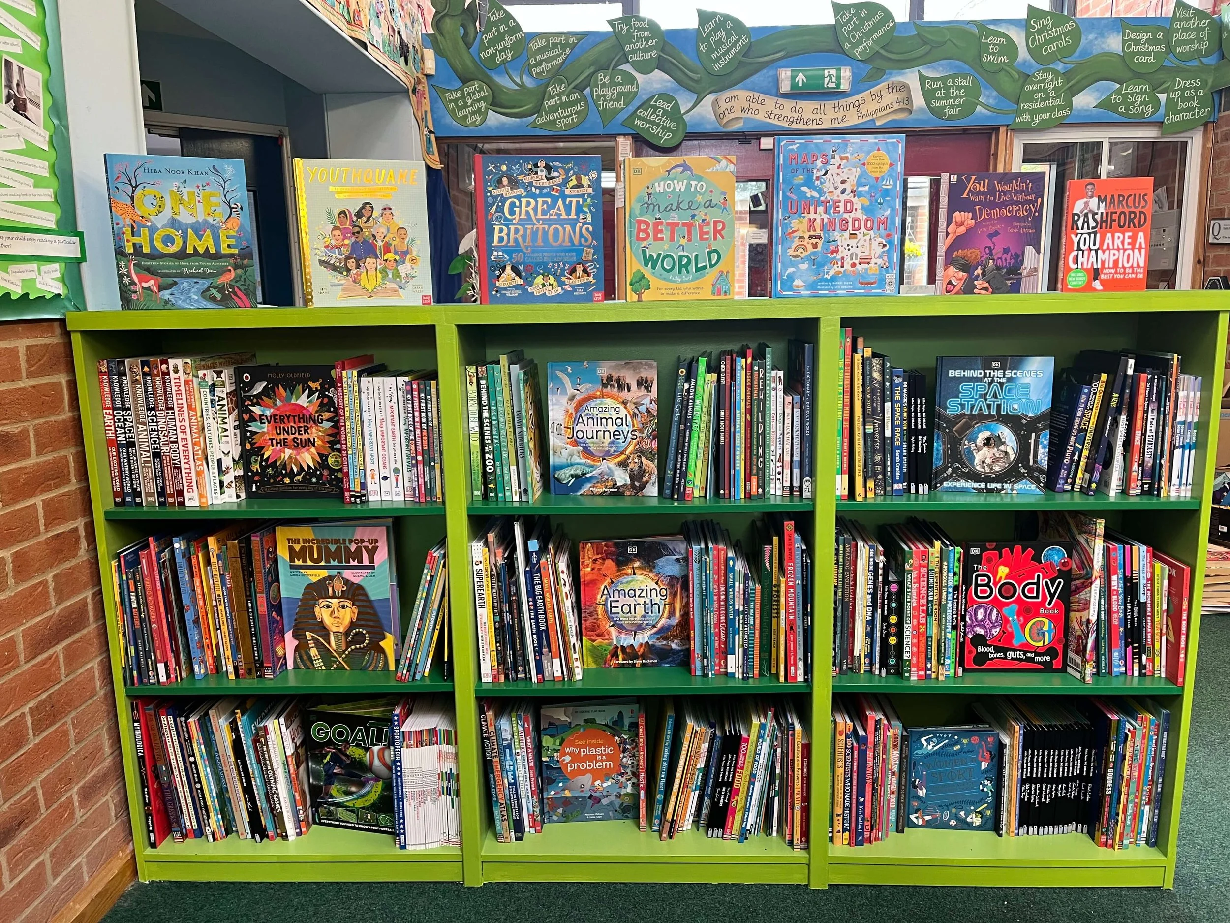 Bookshelf filled with bright and colourful non fiction children's books in a primary school library. The shelves are green and the setting is bright and welcoming.
