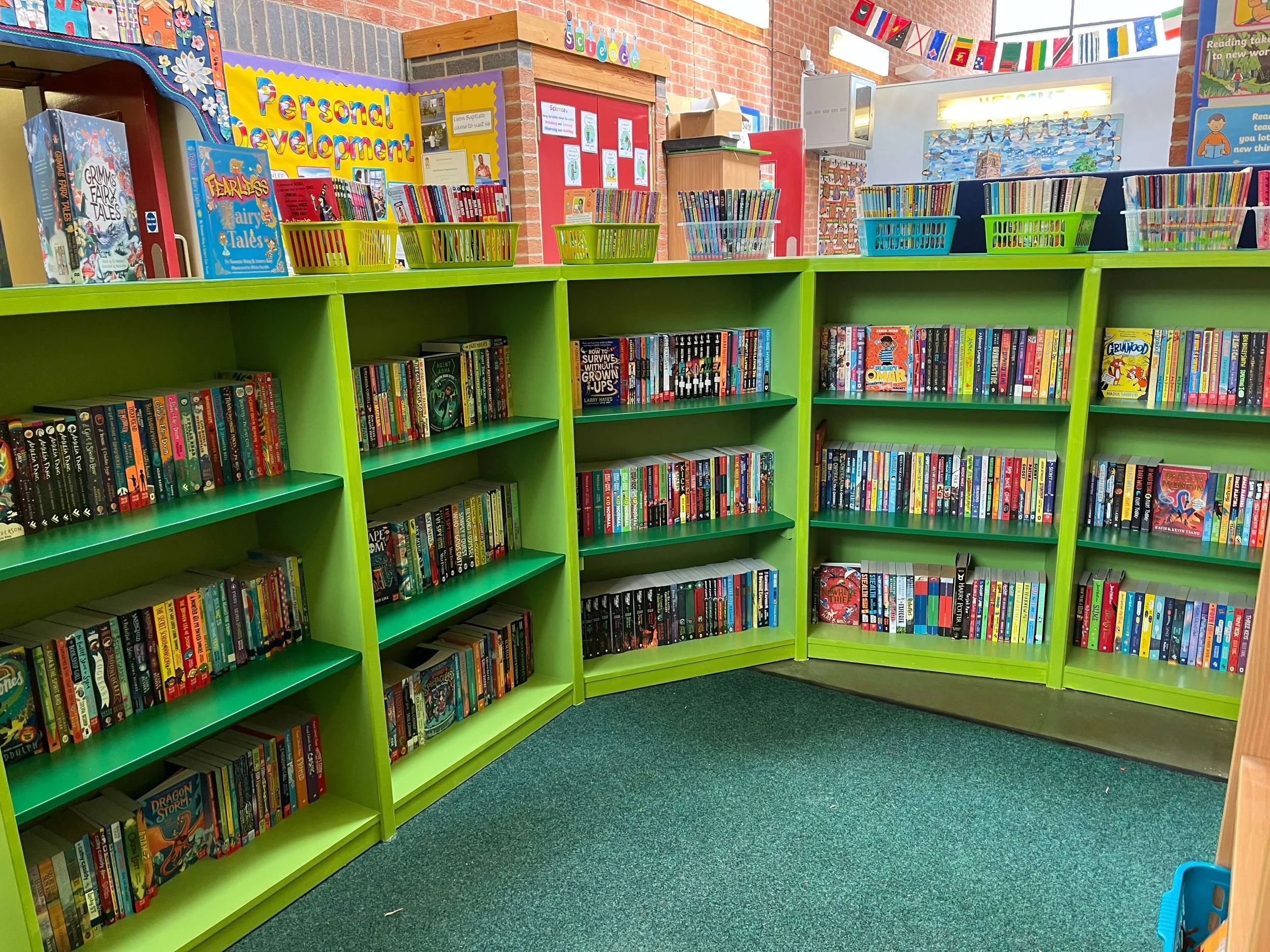 Primary School Library. Colourful shelves filled with modern and diverse fiction books organised alphabetically. 