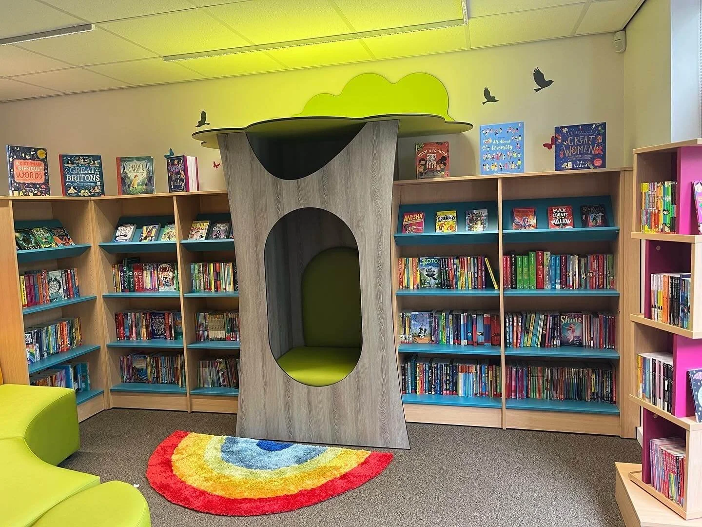 Brand new fiction books displayed in a new primary school library. The books are modern and diverse and organised alphabetically. The primary school library has a reading nook for children to sit in. 