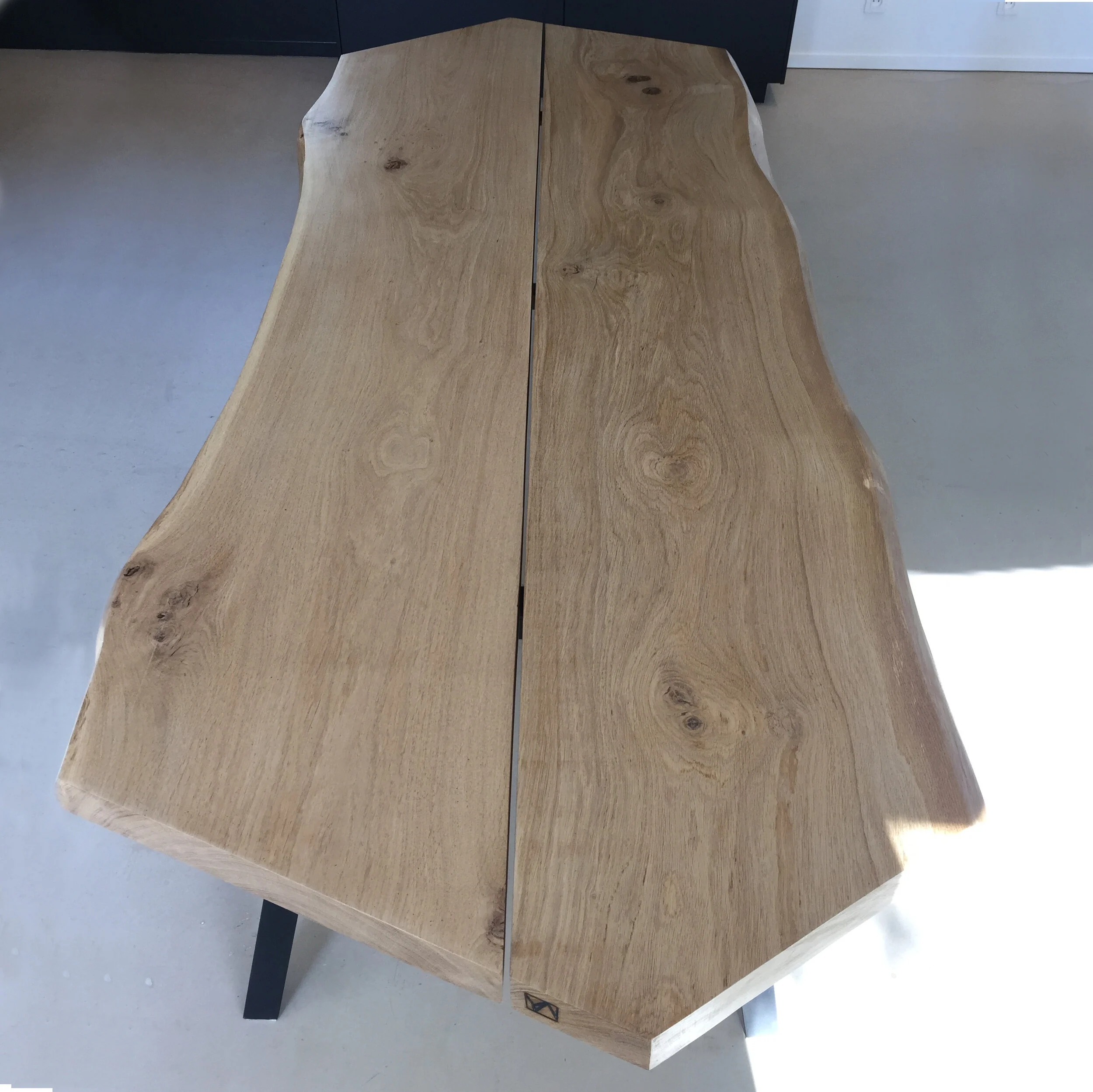 Table en bois de forme irrégulière avec des bords naturels, placée sur un sol en béton et soutenue par une base en métal noir.