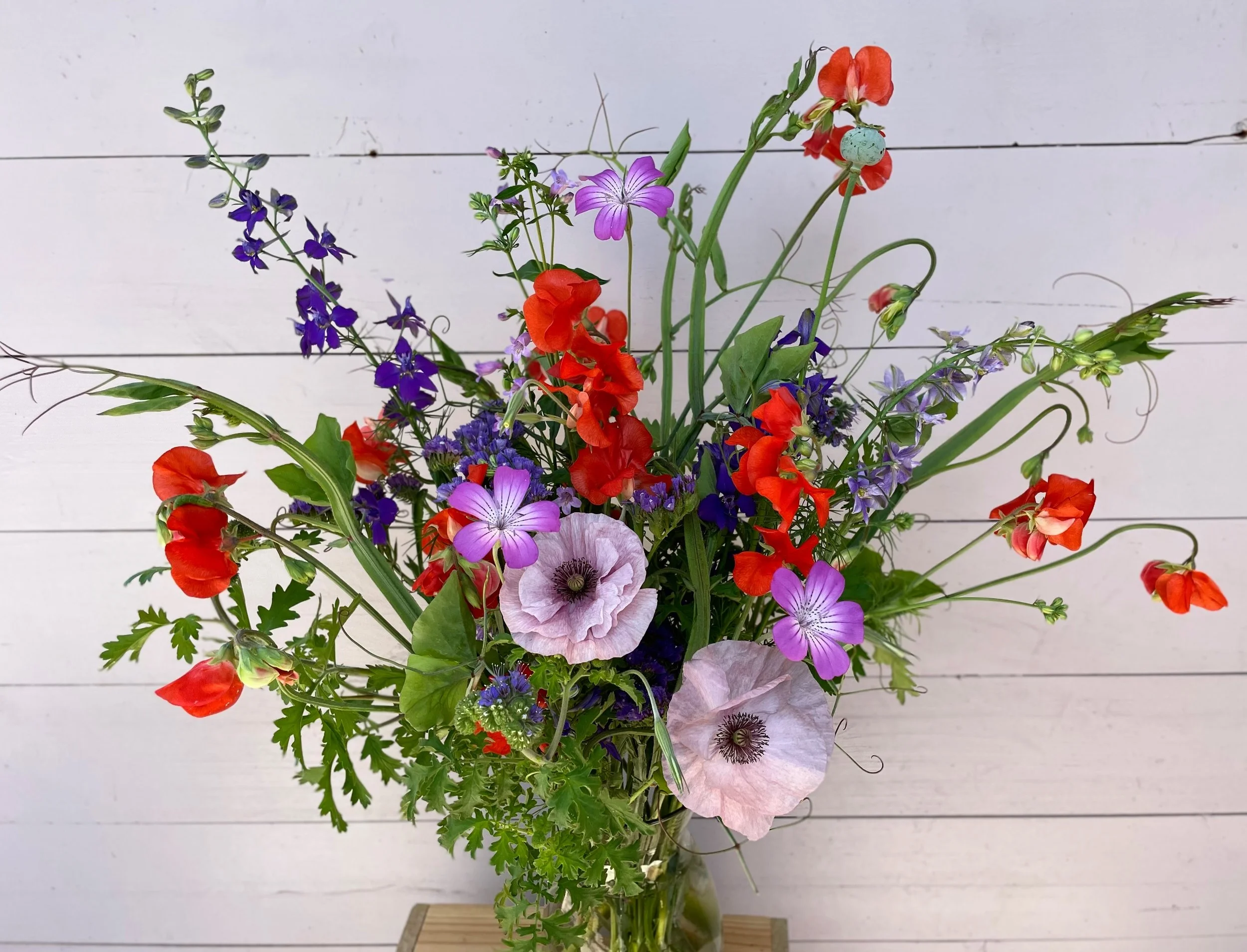 Colorful mixed flower bouquet in a glass vase on a white wooden background.