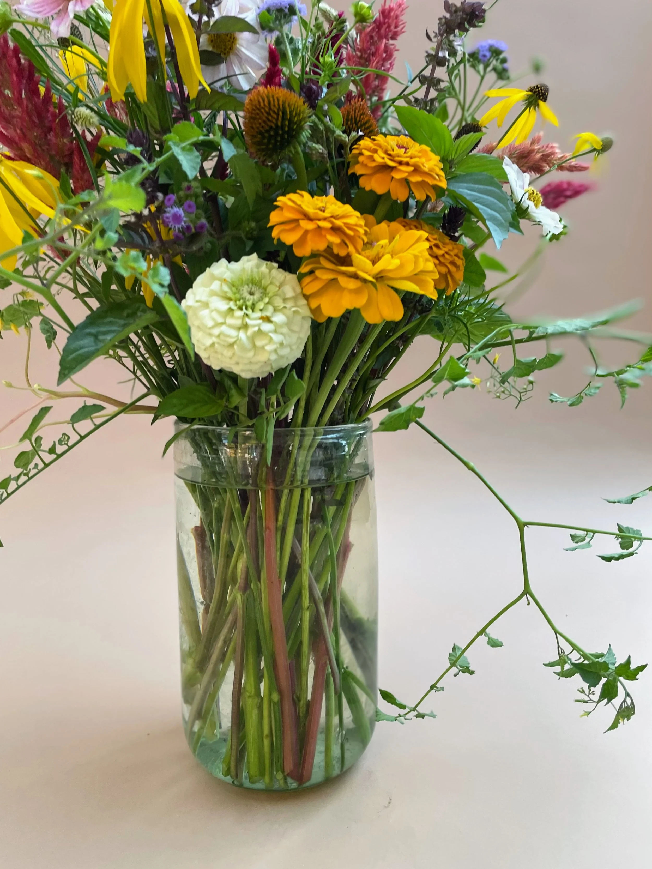 A seasonal bouquet of various colorful flowers in a clear glass vase placed on a light-colored surface.