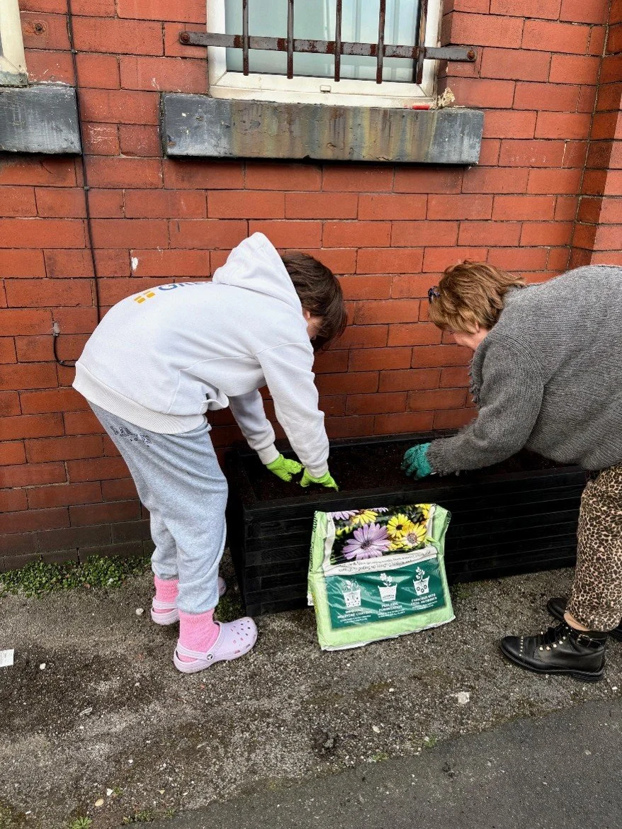 Image shows a young person and a woman potting up an outdoor planter