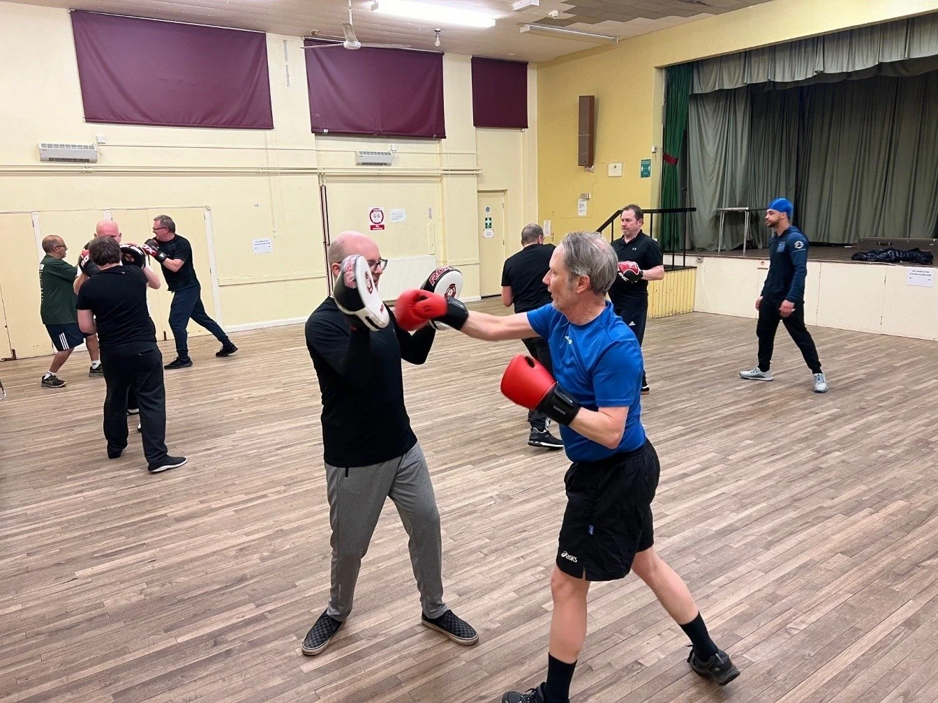 Image shows a group of men sparring, wearing boxing gloves.