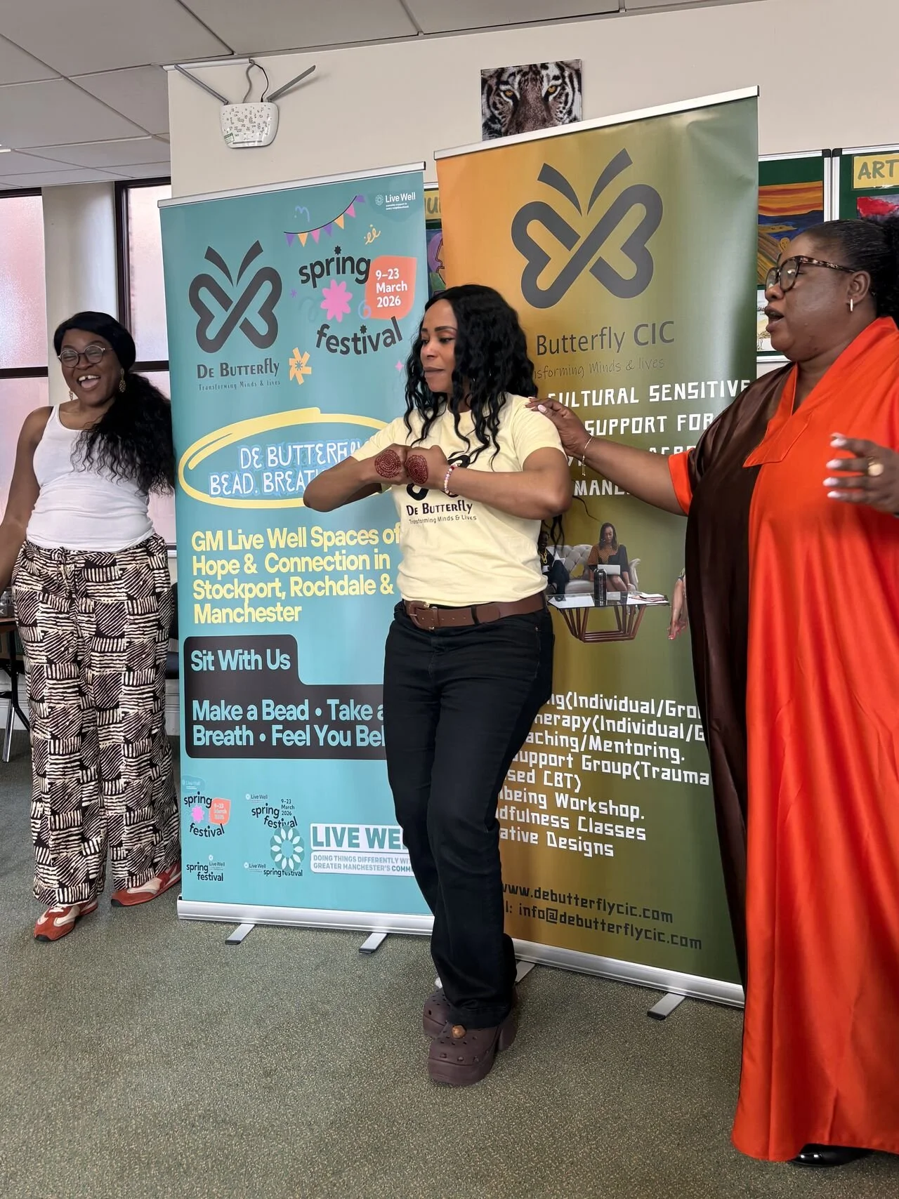 Image shows three women talking to a crowd, stood in front of banners that promote DeButterfly CIC