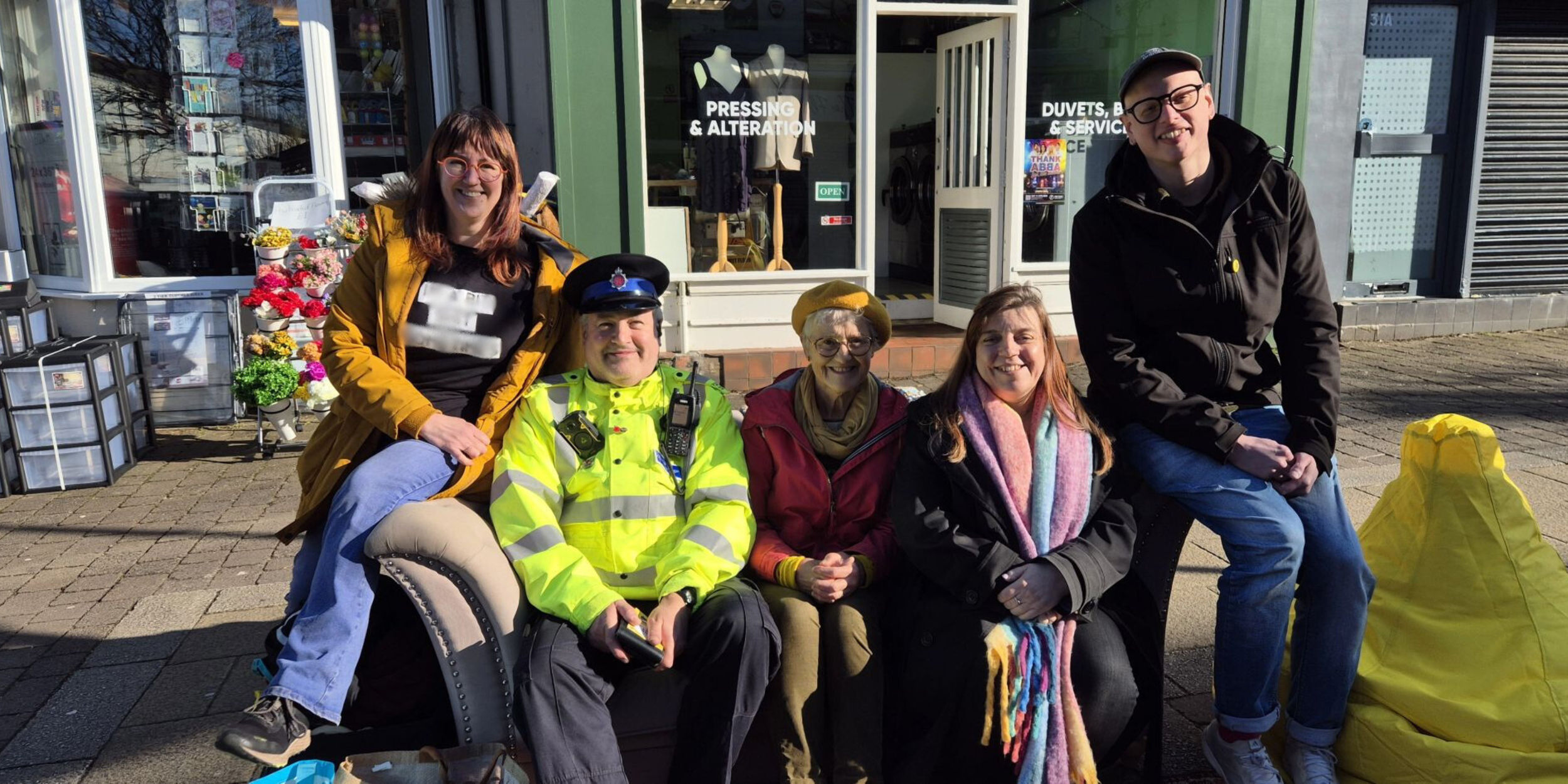 Image shows a group of diverse people sat on a sofa in the middle of Marple High Street