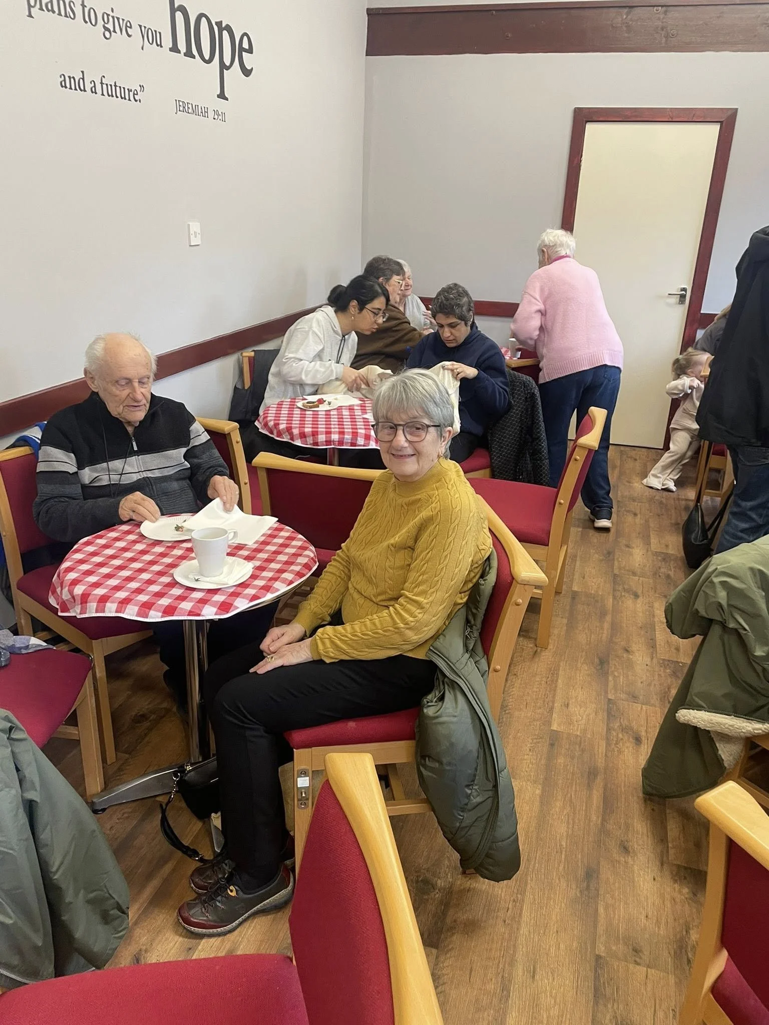 Image shows a group of people sat around tables with cups of tea