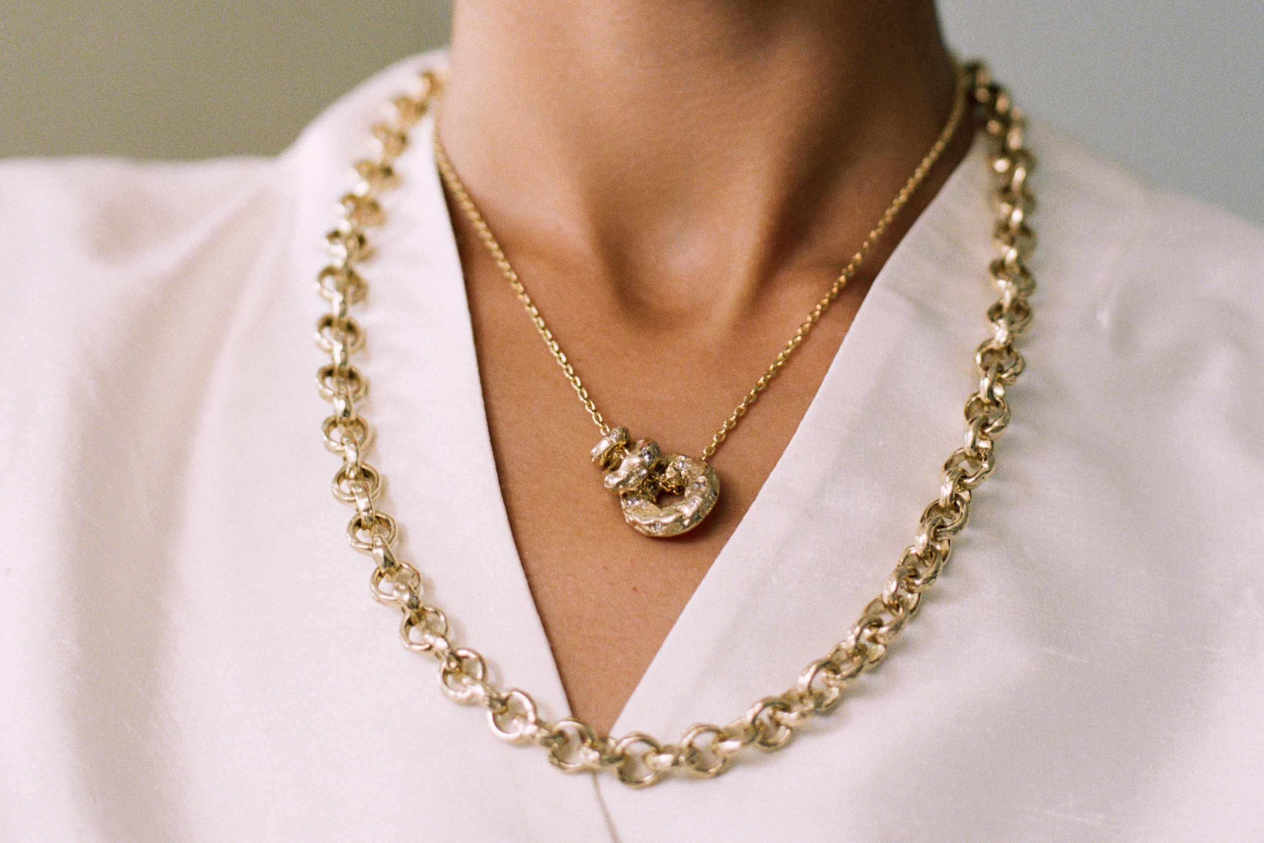 A chain necklace strung with three charms inspired by adder stones, styled with a heavy gold chain - all from the Seun collection by Ellis Mhairi Cameron.