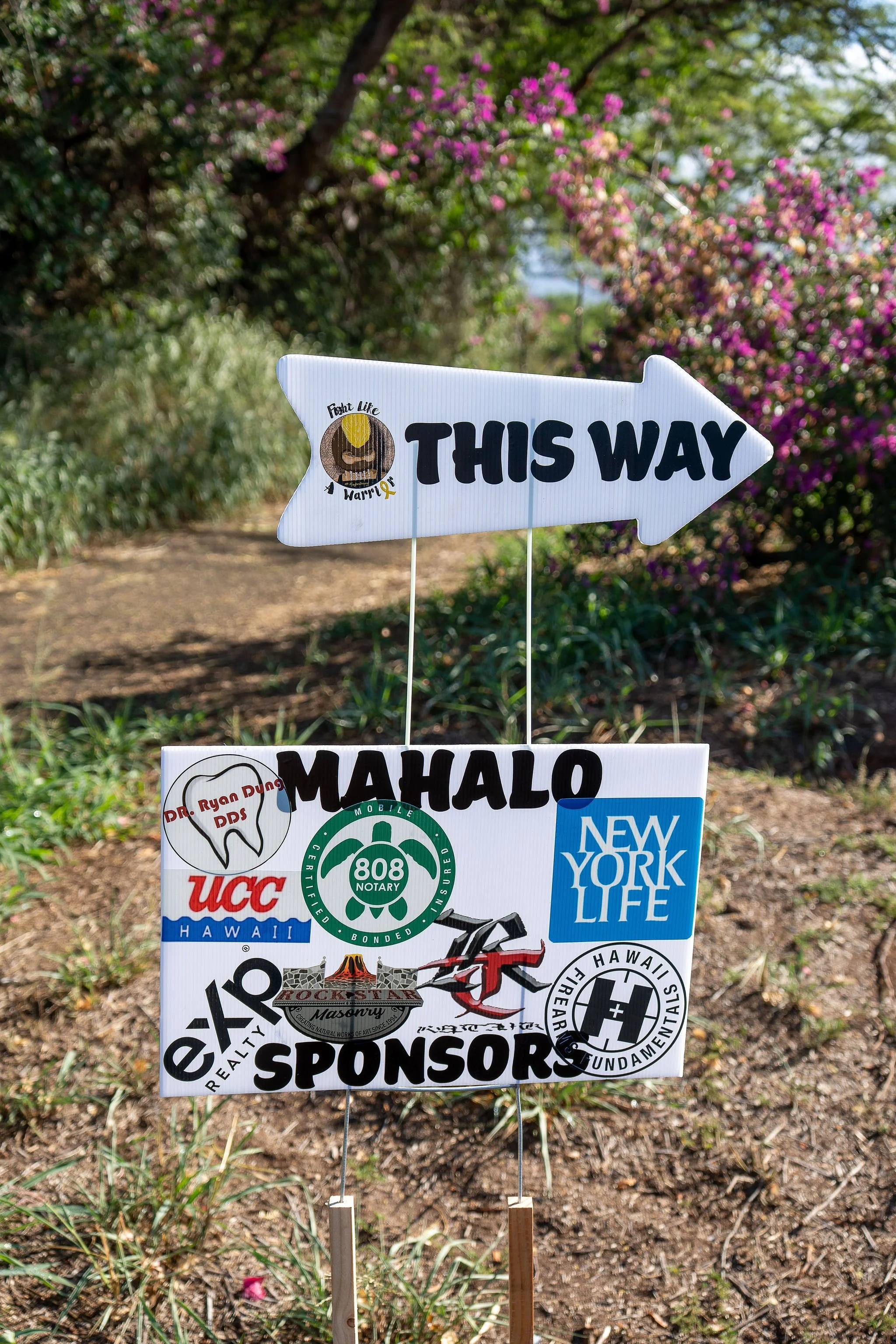 A sign with an arrow pointing right reading 'This Way' and a board below it with various sponsor logos and names, including 'Dr. Ryan Dung, DDS,' 'UCC Hawaii,' '808 Notary,' 'New York Life,' 'Rockstar Masonry,' 'Hawaii Firefighters,' and 'Hawaii Fund
