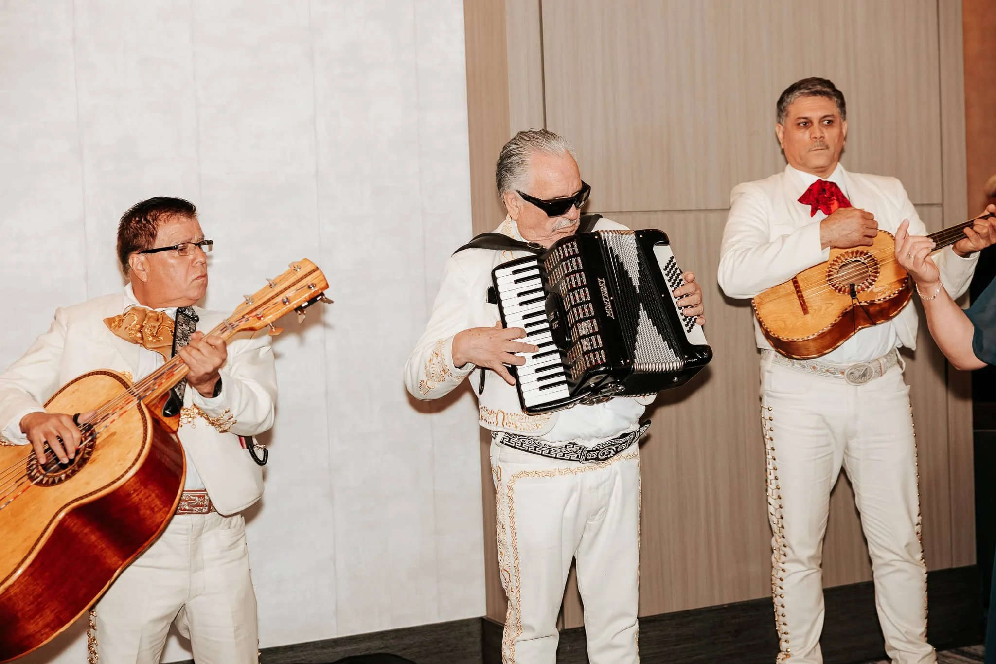 Three mariachi musicians in white outfits playing guitar and accordion at a wedding